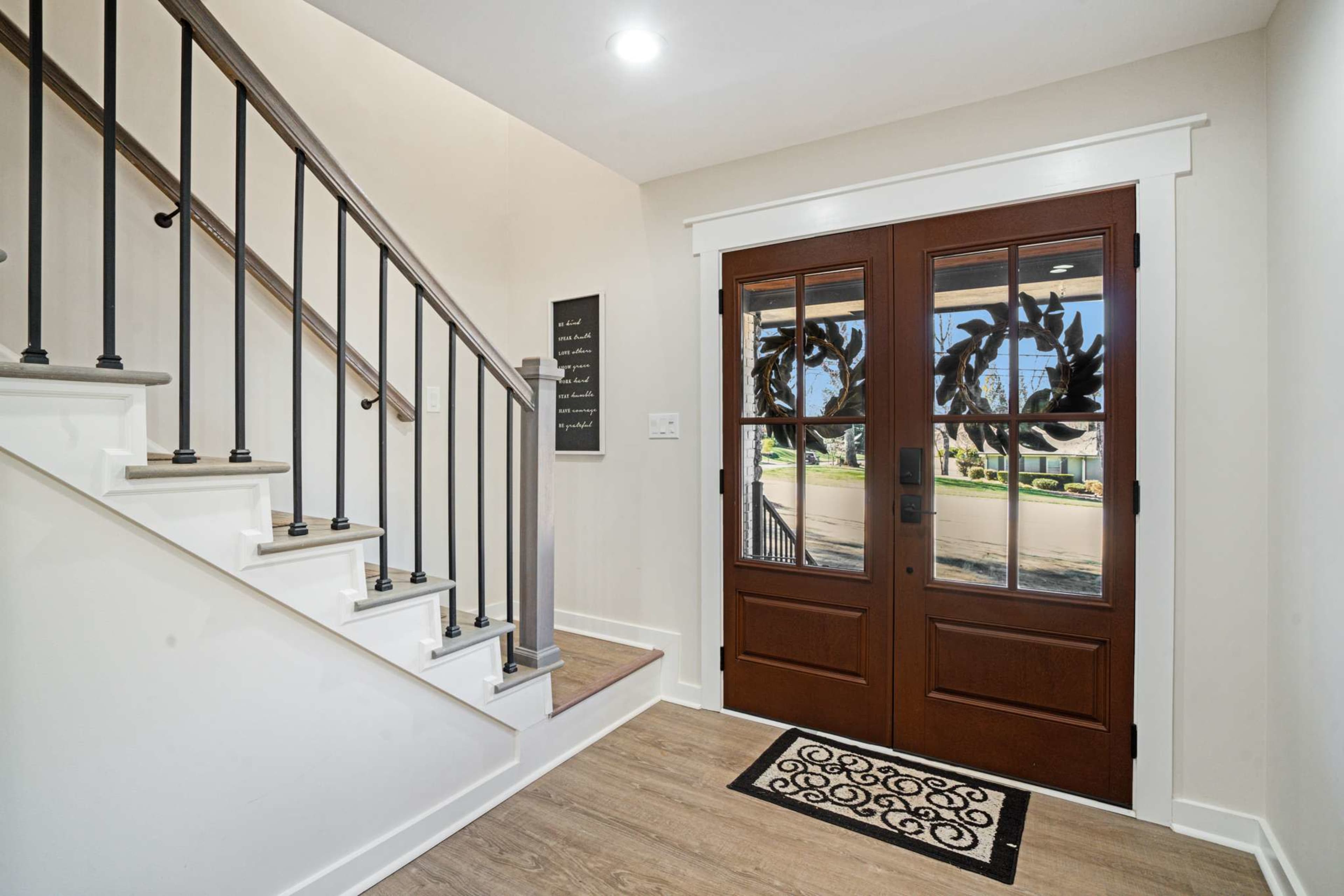 The image shows a front entryway with a dual door, a staircase to the left, and a decorative rug on the floor.