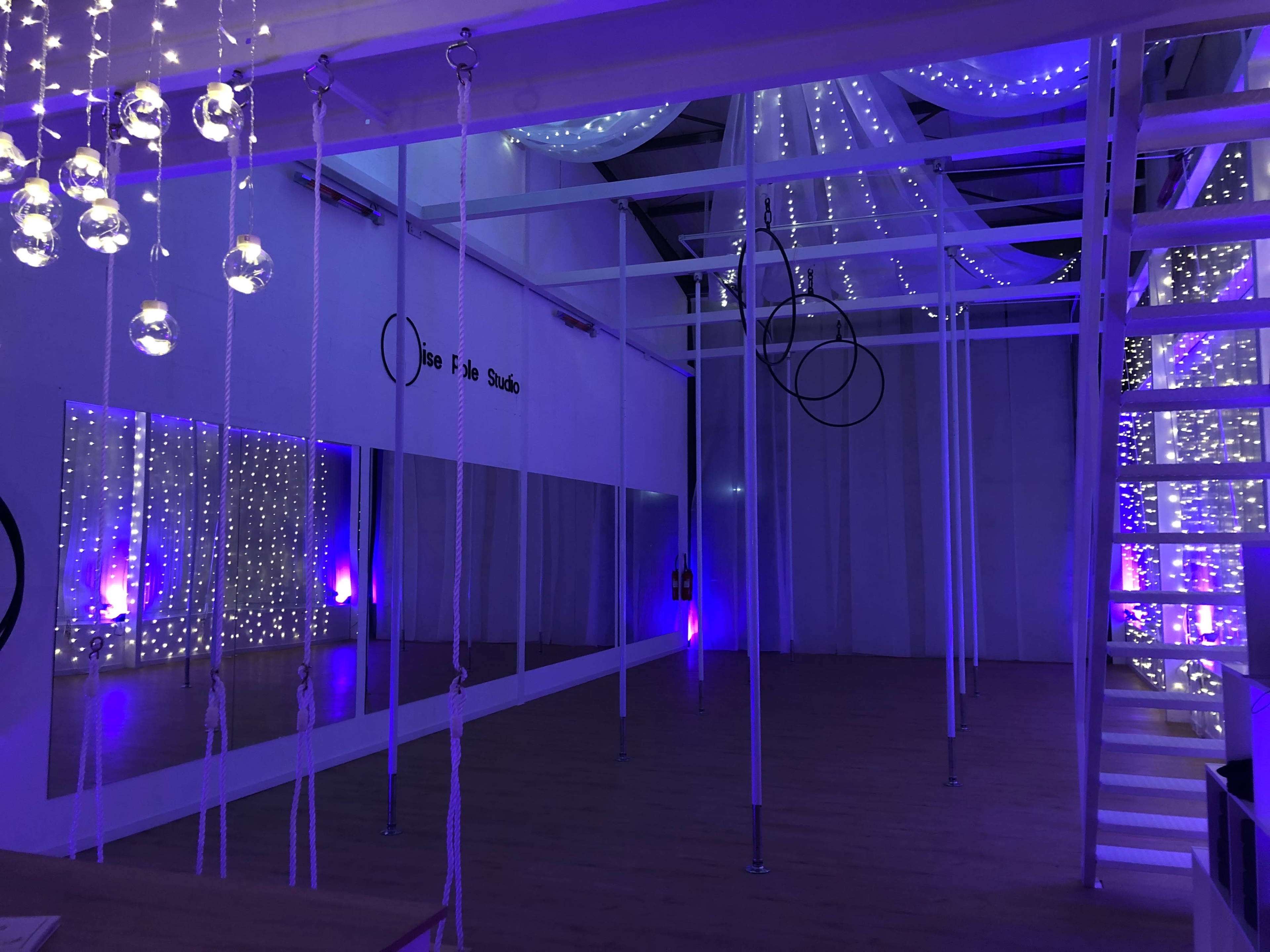 A studio space with ropes hanging from the ceiling, large mirrors on one wall, and decorative fairy lights creating a soft glow.