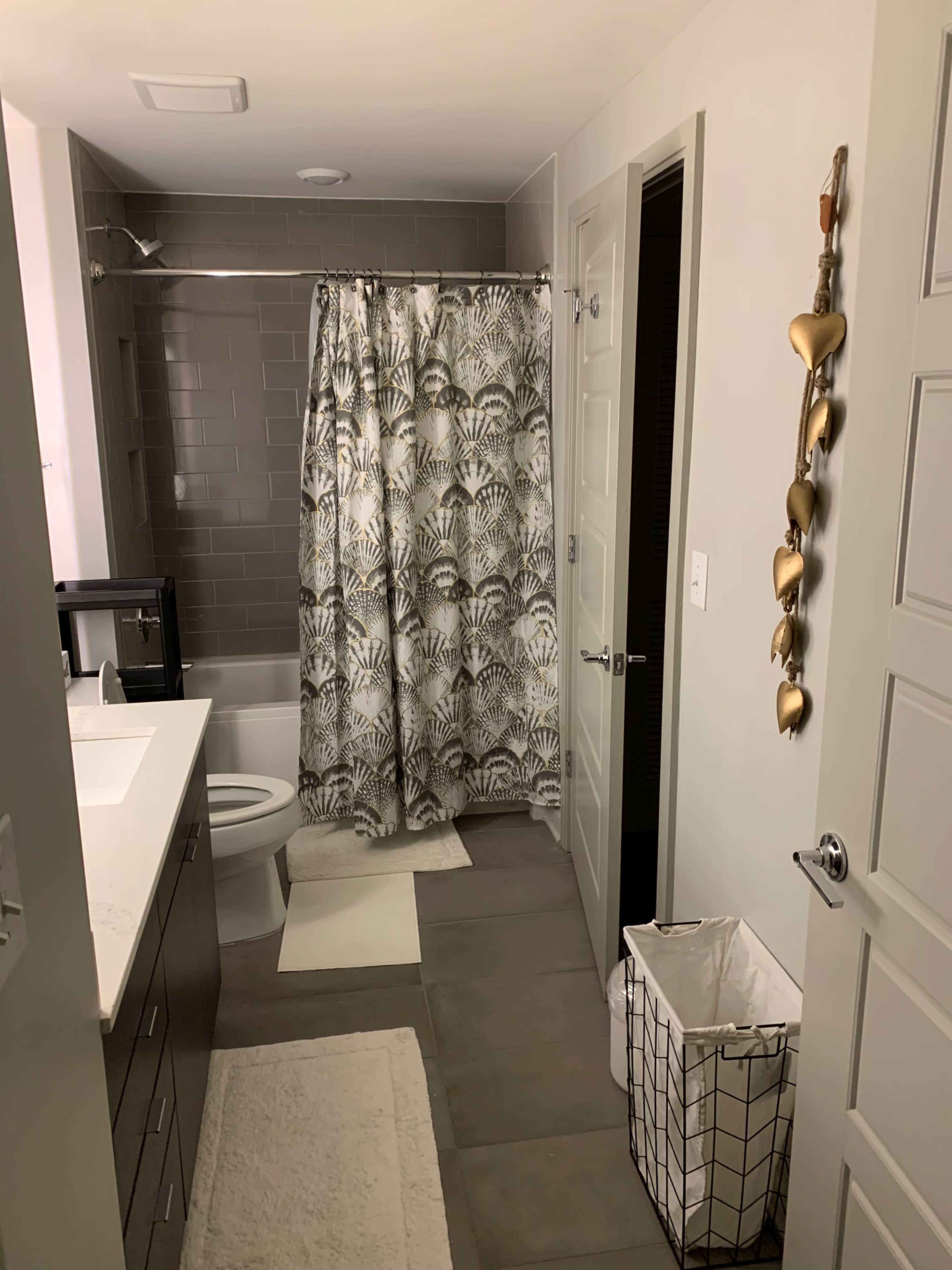 A modern bathroom featuring a shower with a patterned curtain, a toilet, a sink with a countertop, and a laundry basket.
