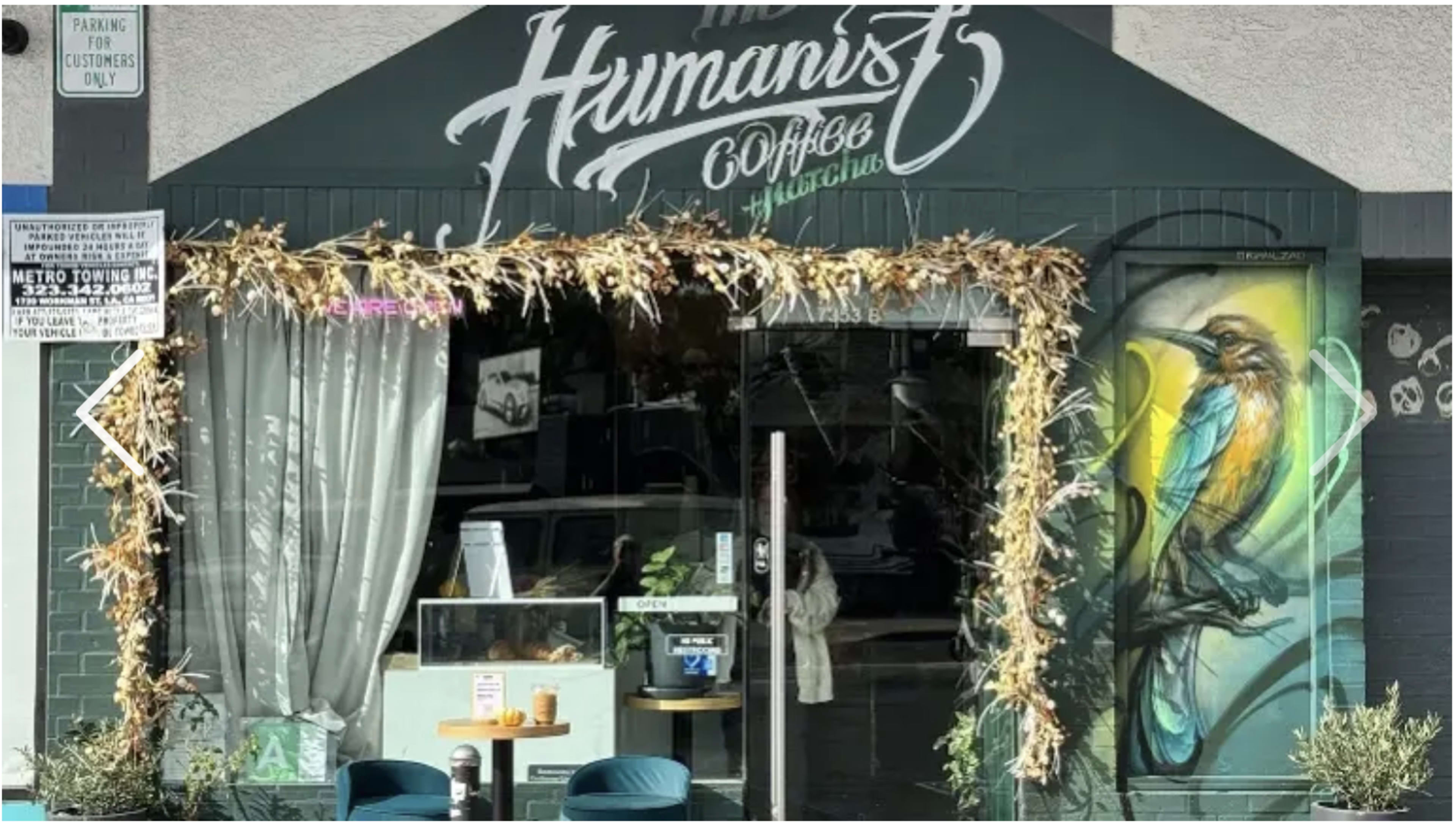 The image shows the entrance of a coffee shop named "The Humanist," featuring a colorful bird mural and floral decorations around the doorway.