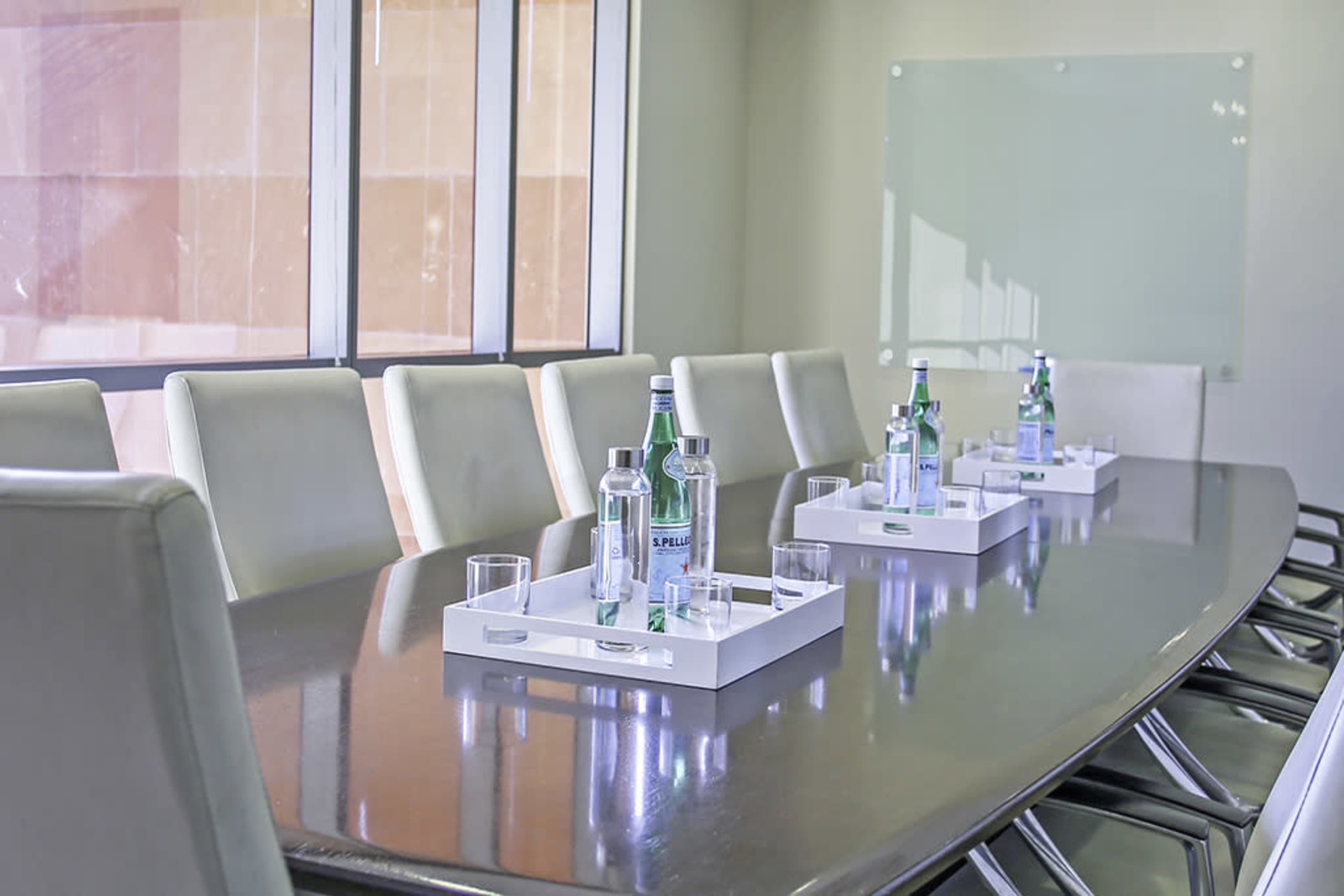 A long conference table is set with water bottles and glasses for a meeting in a brightly lit room.