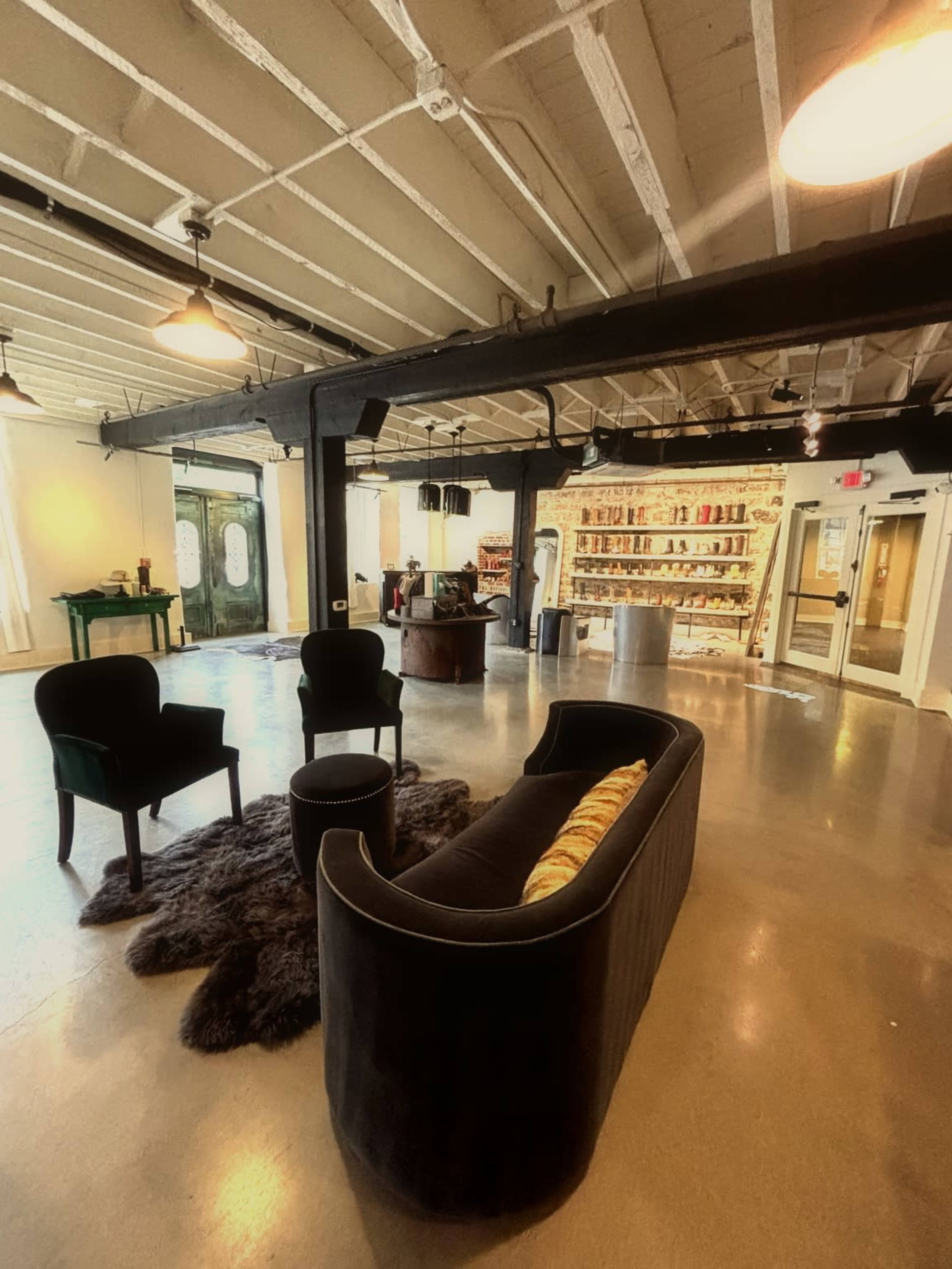 The image shows a spacious interior with modern furniture, featuring a dark sofa, chairs, and a display of products on shelves in the background.