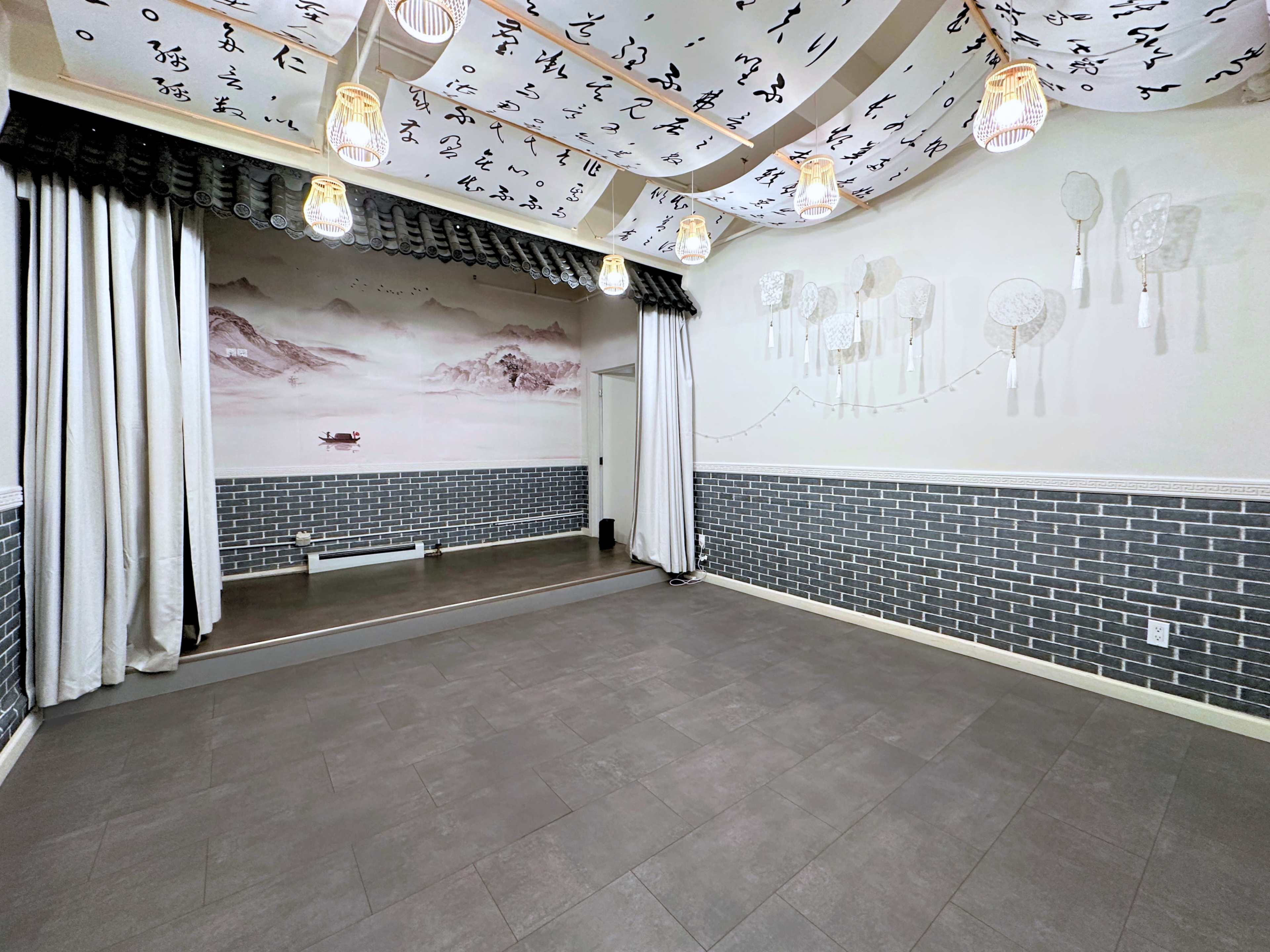 The image shows a spacious room with a large mirrored wall, featuring decorative paper lanterns and a painted mural of mountains on one side.