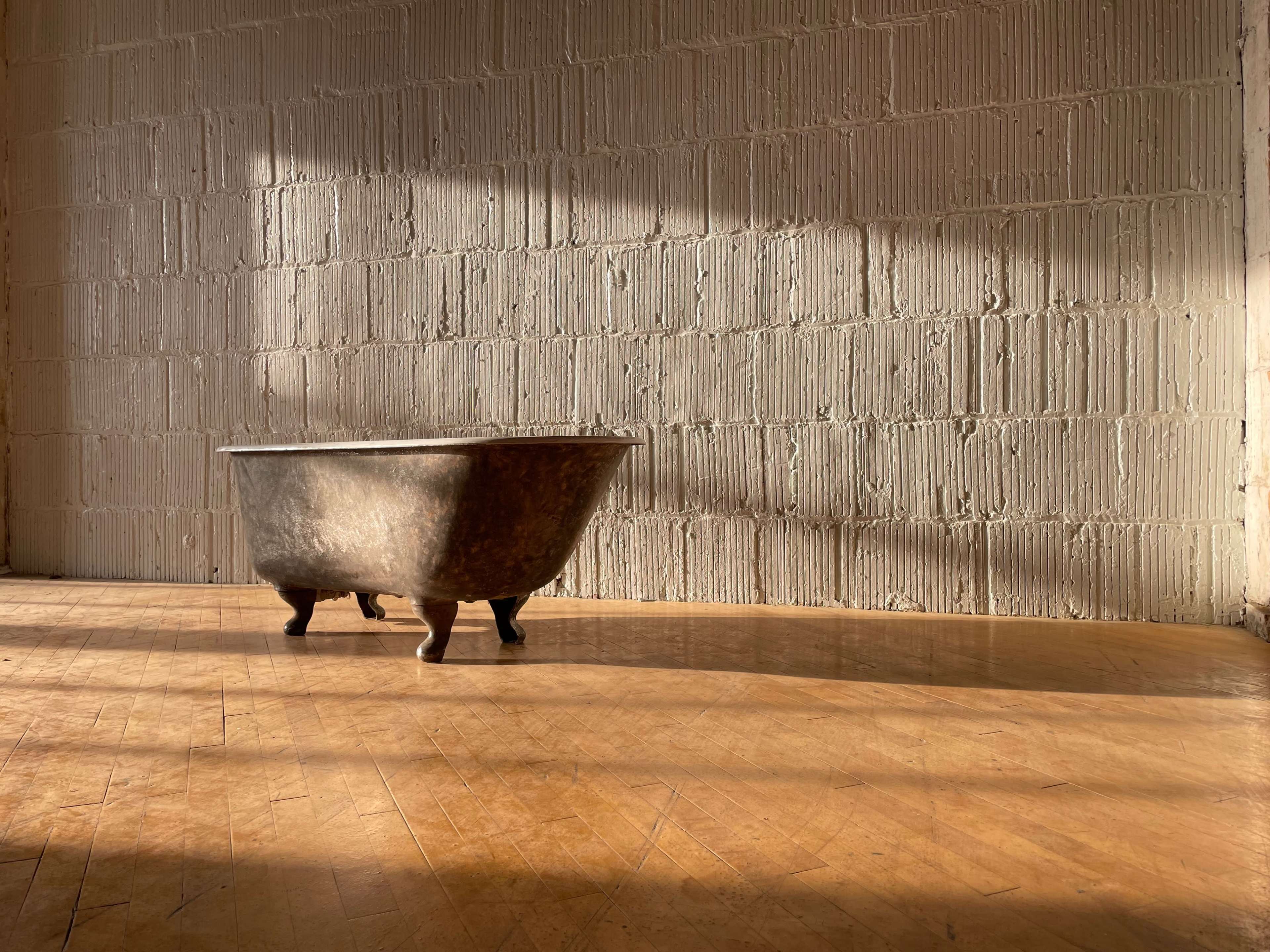 A vintage bathtub is positioned in a sunlit room with a textured wall and wooden flooring.