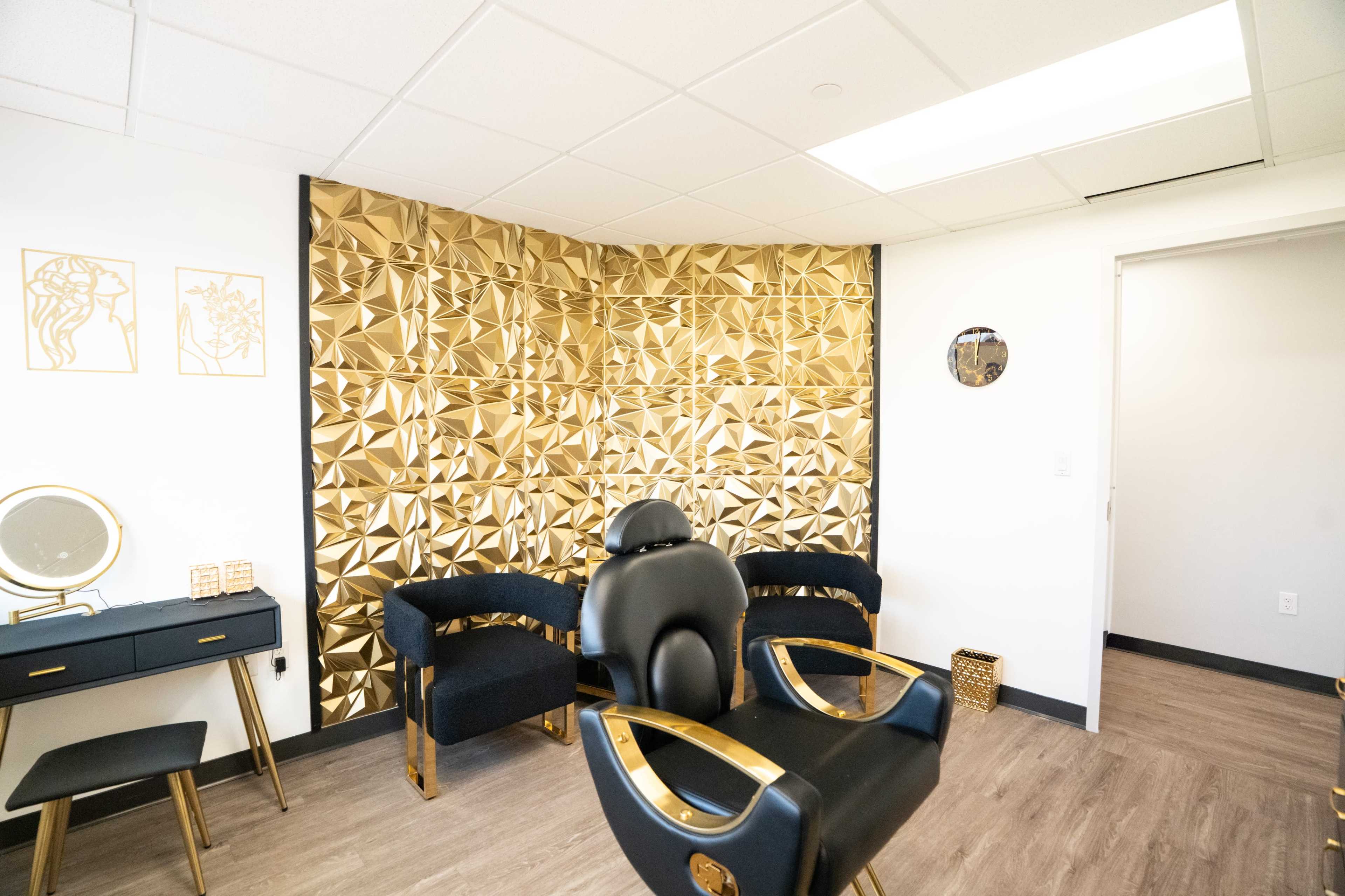 The image shows a modern beauty salon interior featuring golden geometric wall panels, a black chair, and a black vanity with a circular mirror.