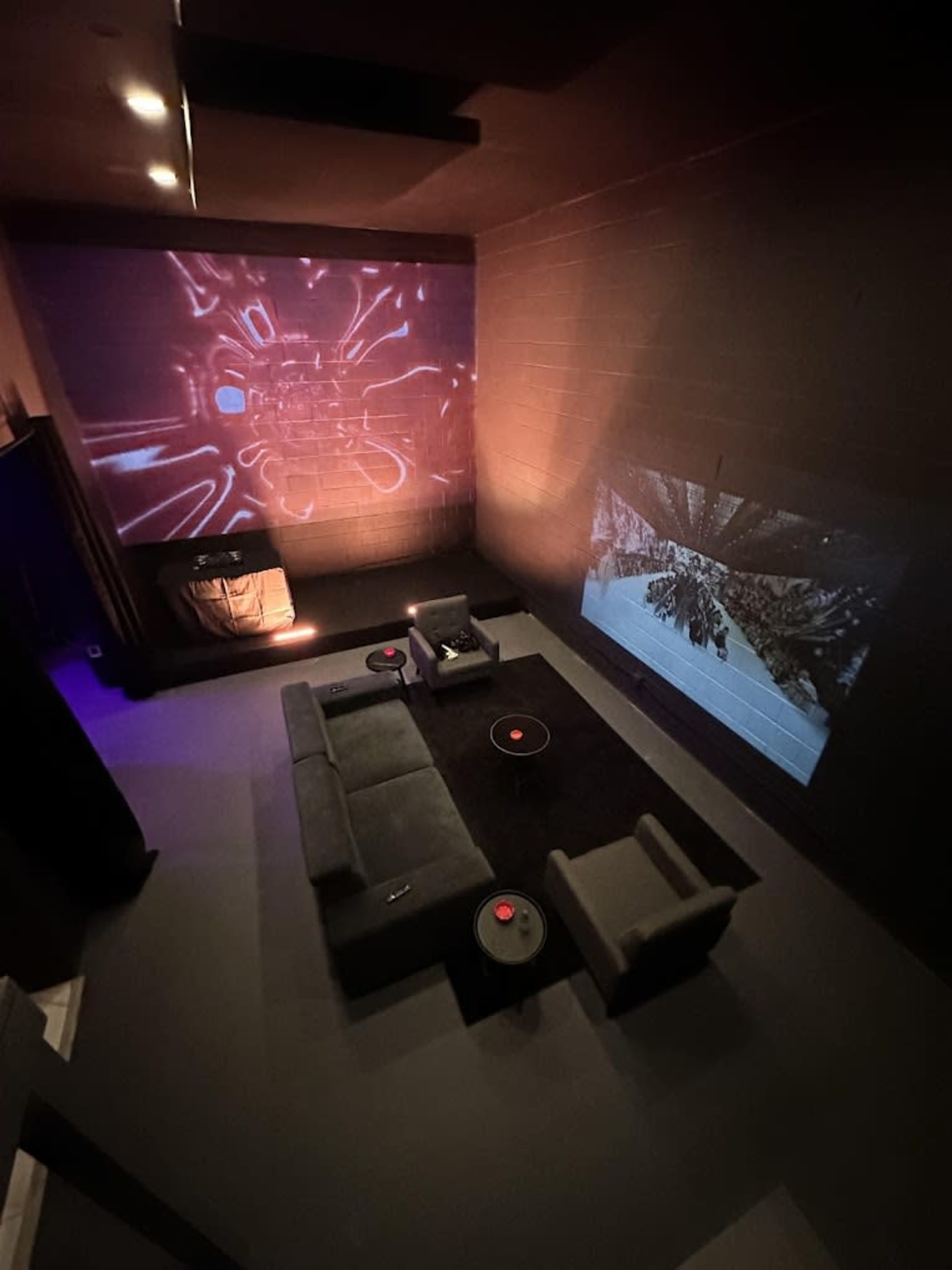 A modern home theater features large projection screens displaying dynamic visuals, with comfortable seating arranged in front and ambient lighting.