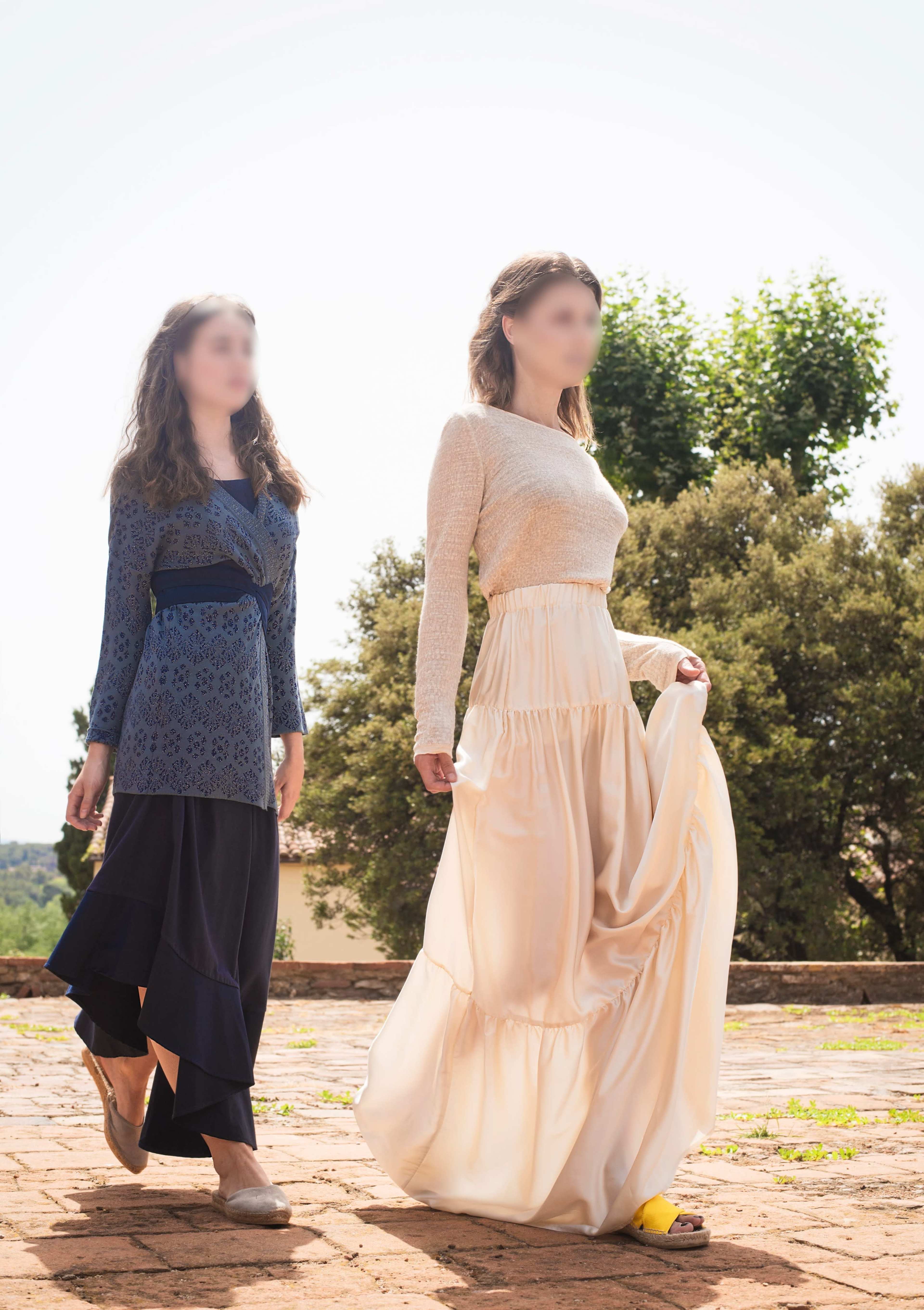 Two women walk along a pathway, one in a patterned blue dress and the other in a light-colored flowy skirt and top.