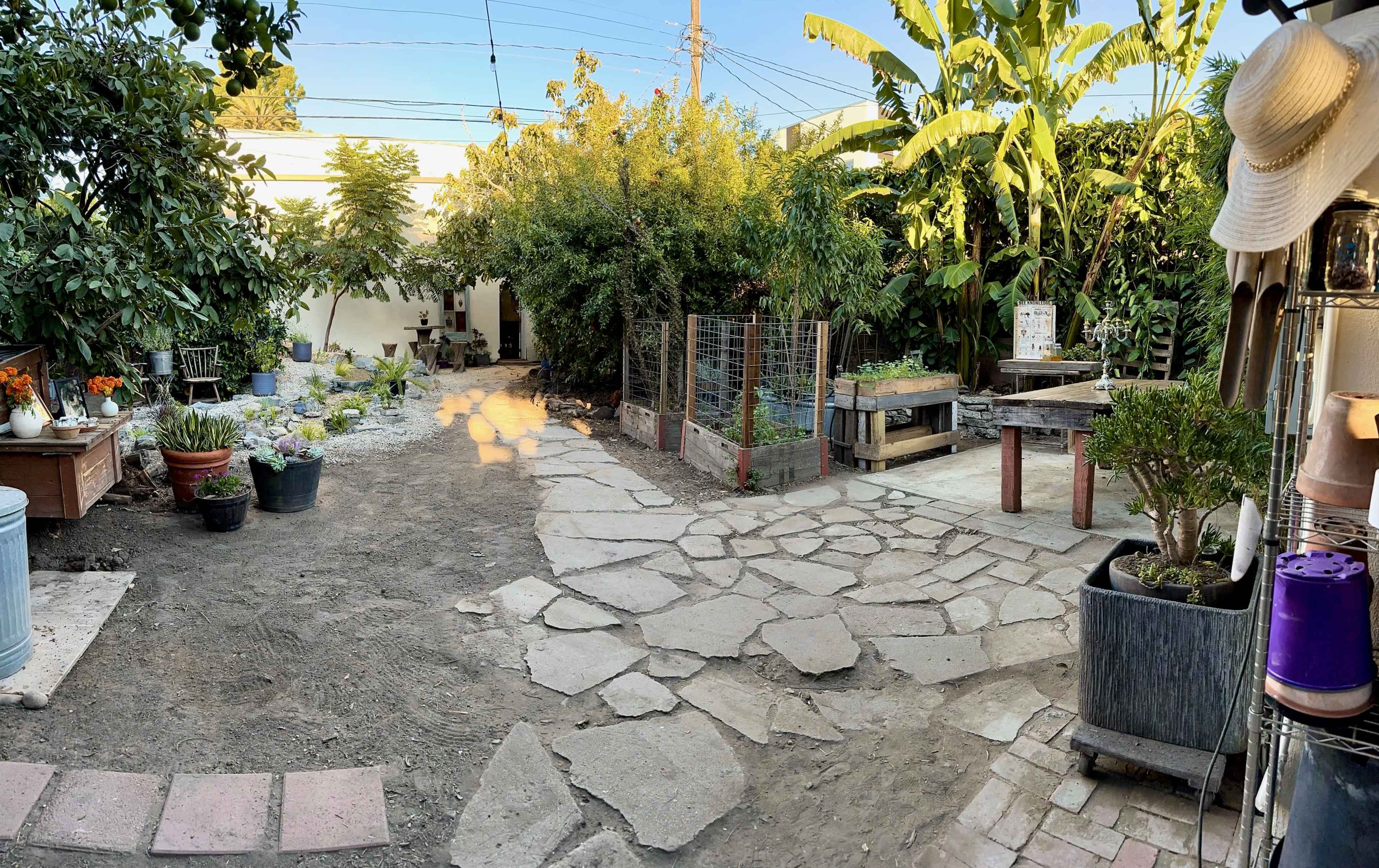 A landscaped garden path made of stone, bordered by various plants, trees, and garden beds.