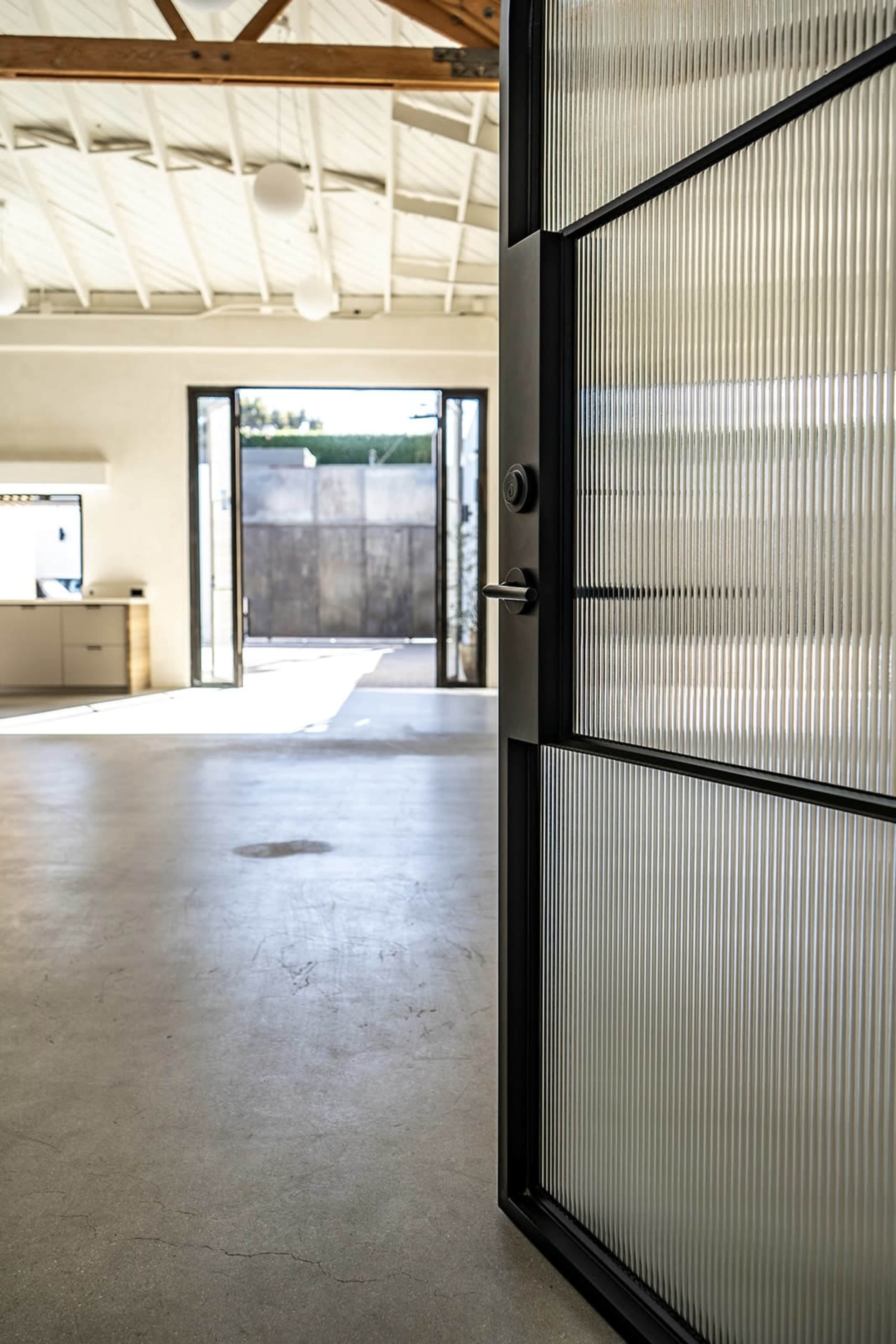 A large glass door partially opens to reveal a spacious interior with high ceilings and natural light streaming in.
