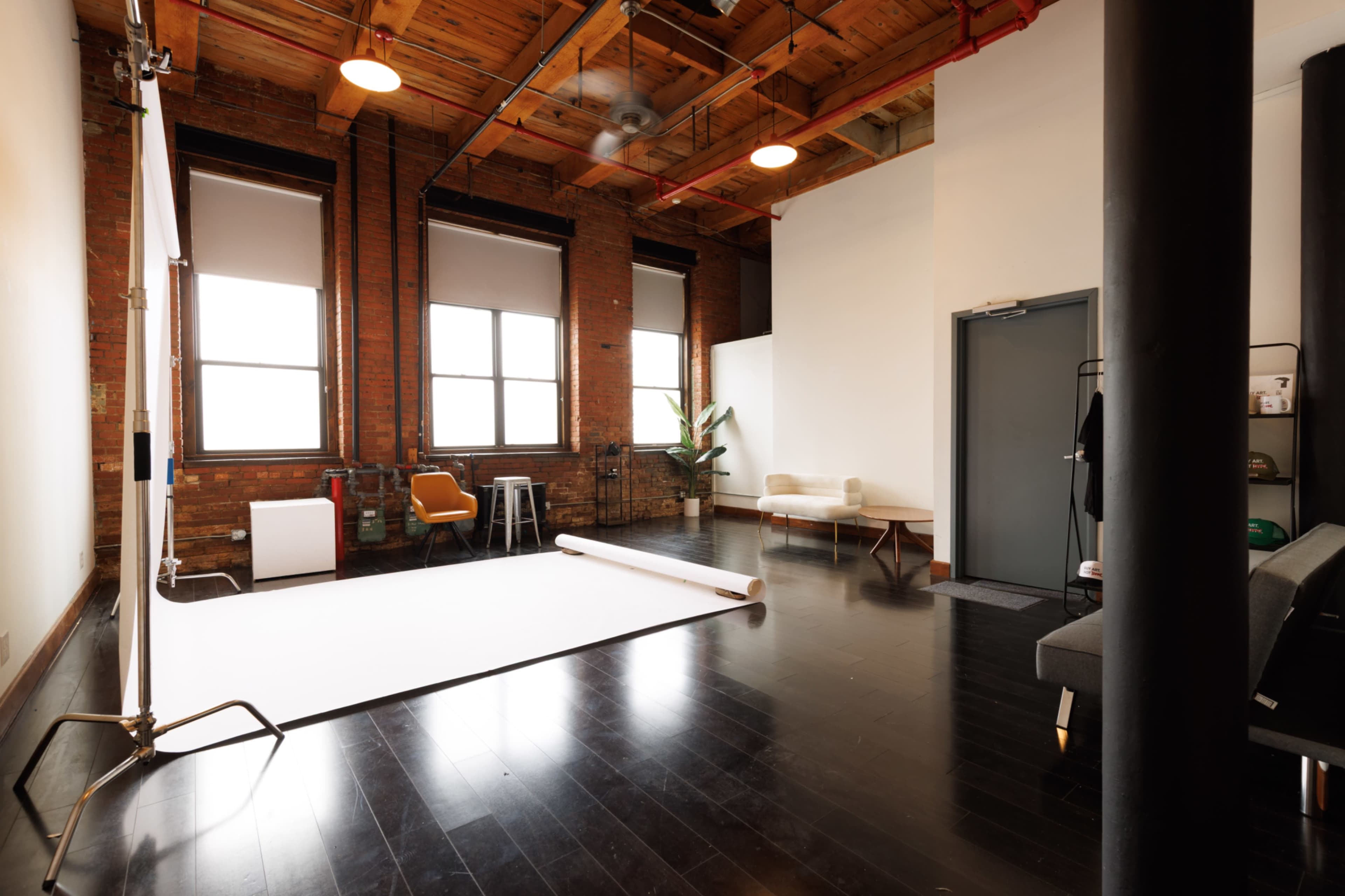 The image shows a spacious, well-lit photography studio with a white backdrop, large windows, and wooden beams in the ceiling.
