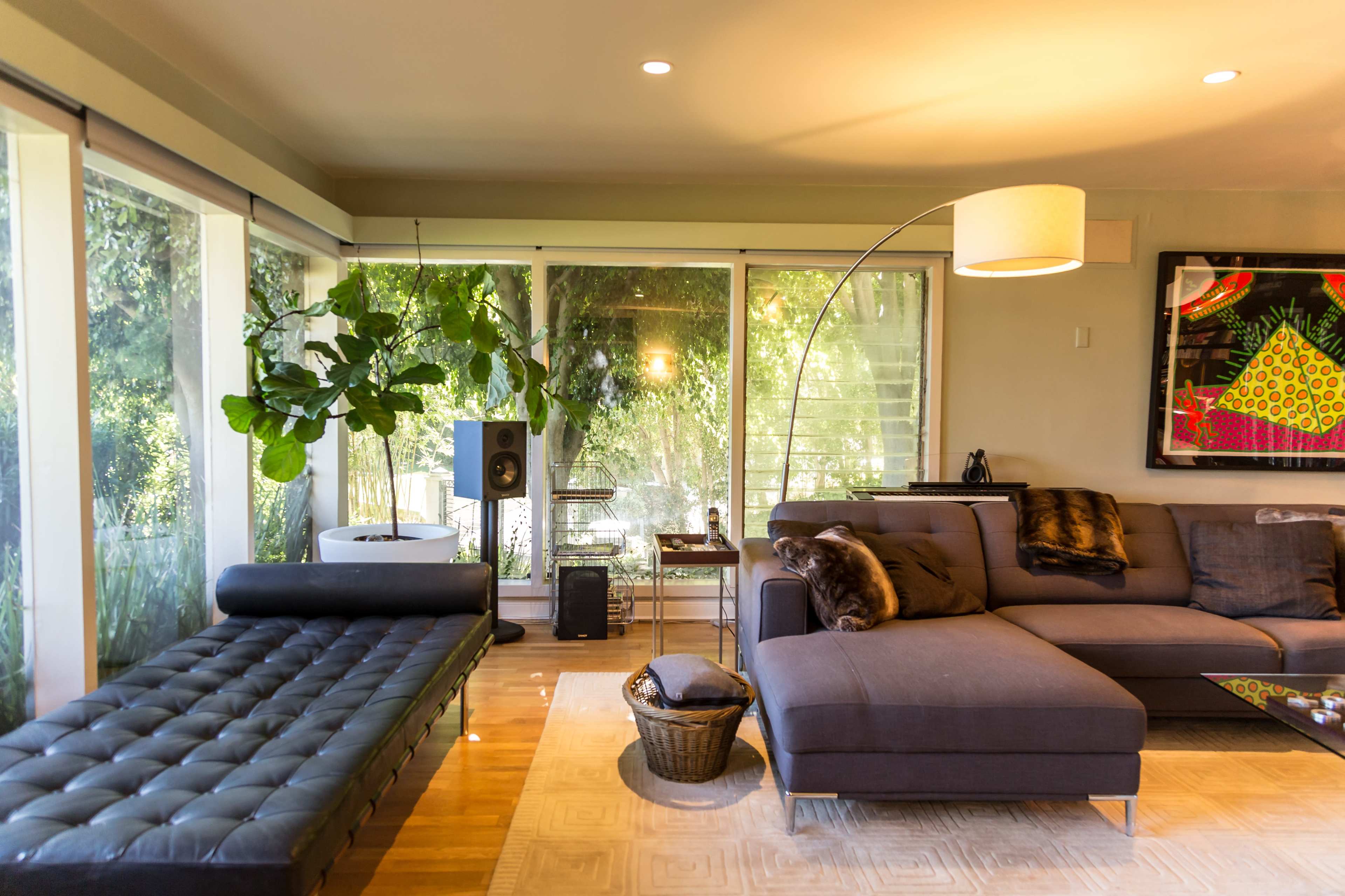 A modern living room with a sectional sofa, a lounge chair, a large window with greenery outside, and an arc floor lamp.