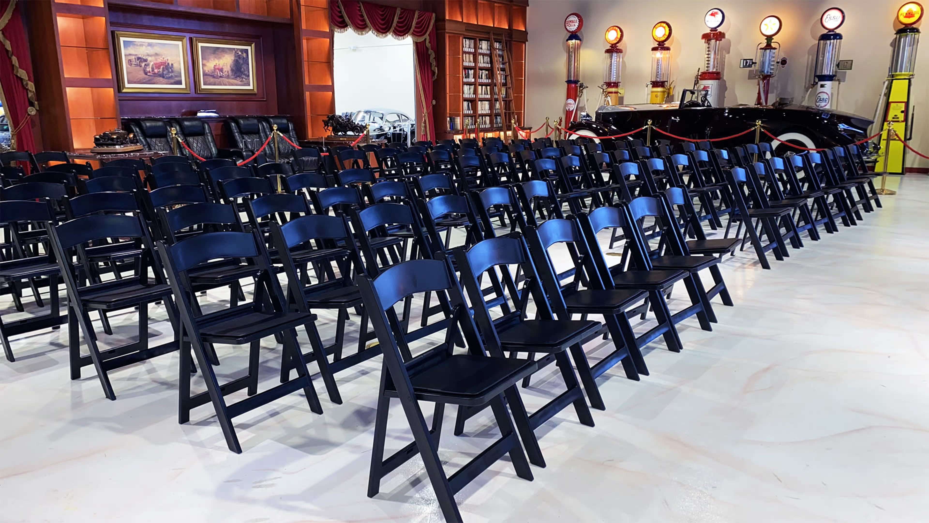 A row of black folding chairs is set up in a spacious room with decorations and vintage gas pumps in the background.