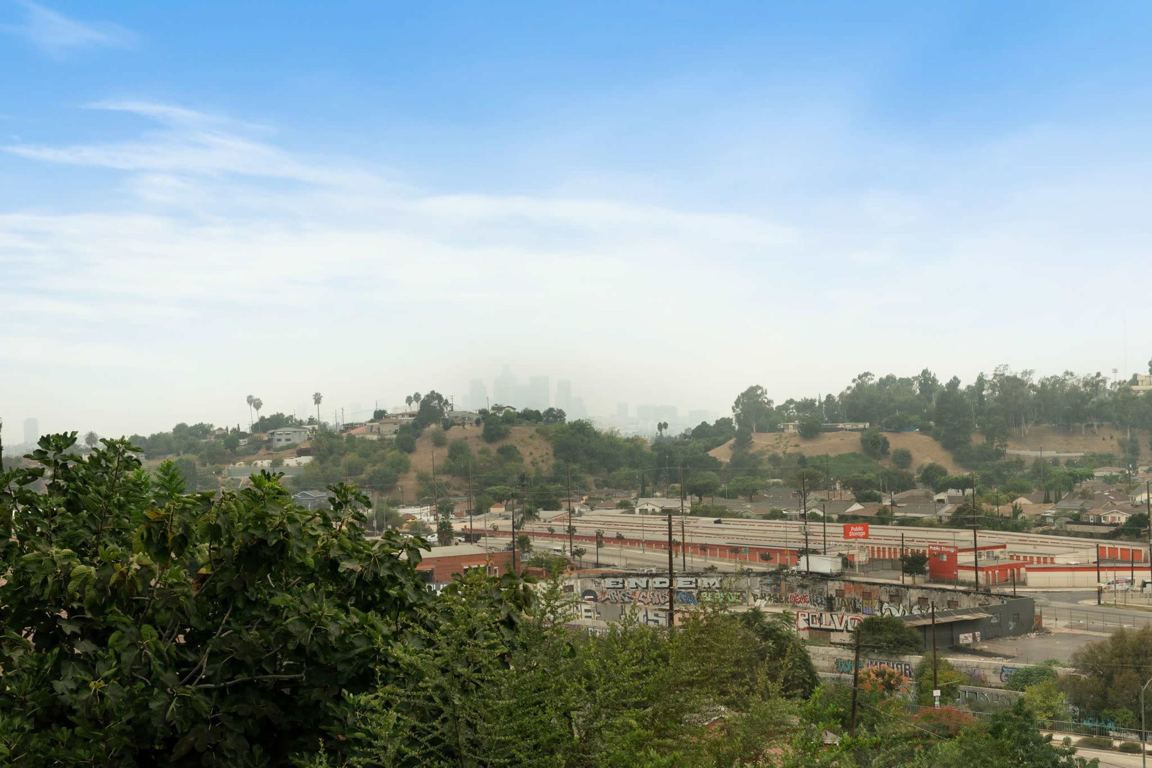 A view of an urban landscape with buildings and roads, partially obscured by haze, against a backdrop of a clear sky.