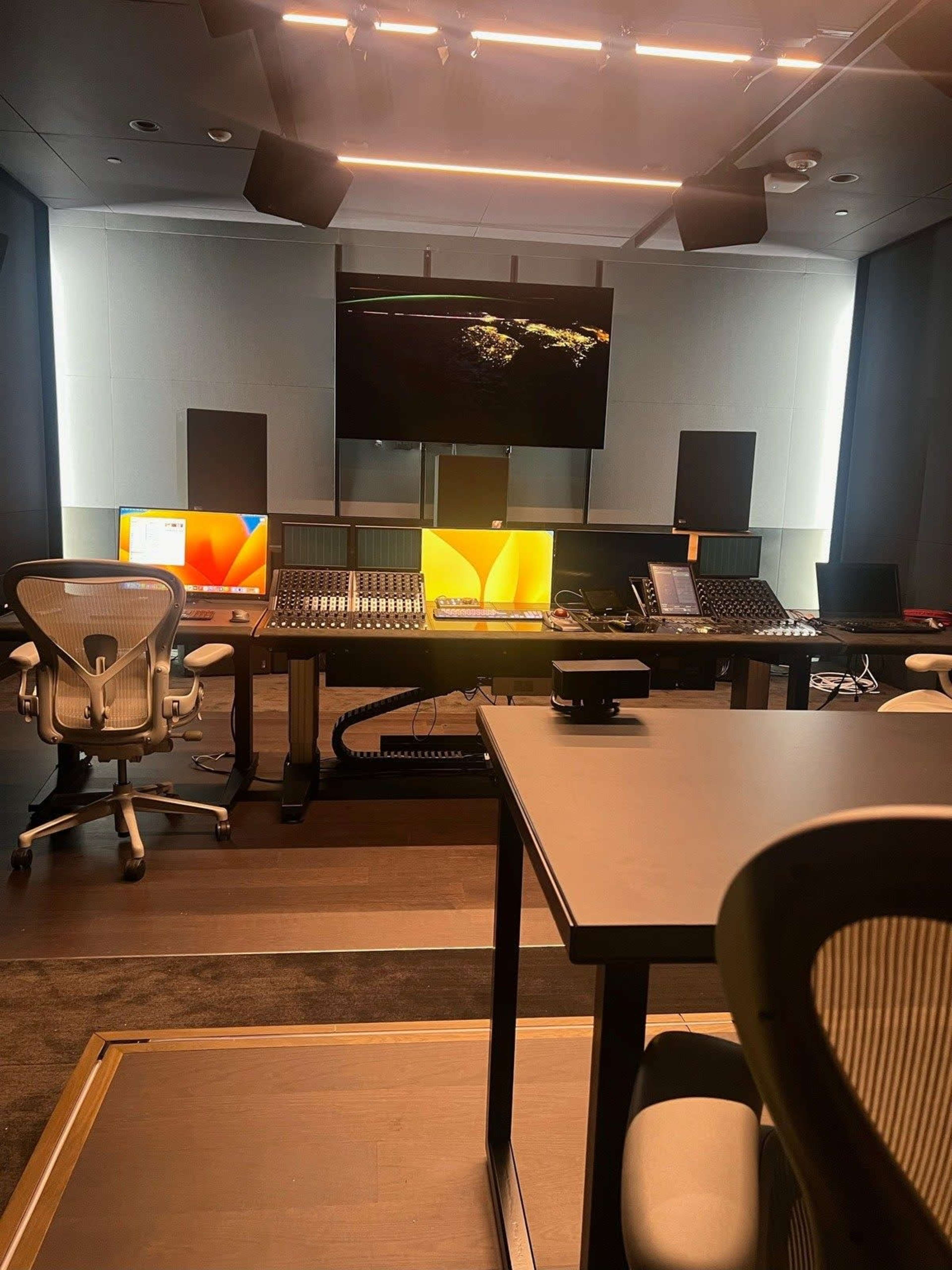 The image shows a modern audio mixing studio equipped with multiple computer monitors, a large mixing console, and studio speakers, all arranged in a sleek, professional setting.