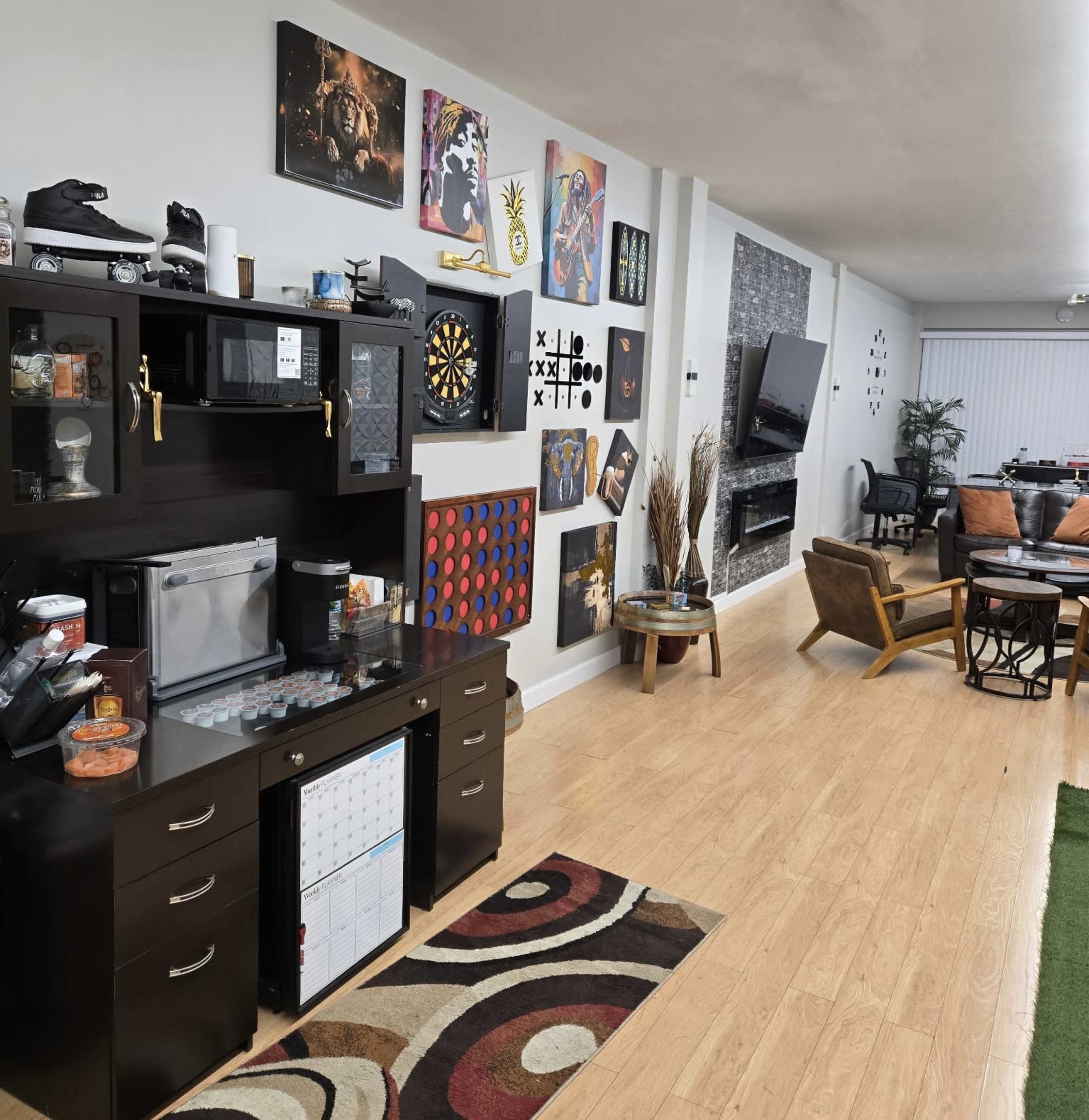 A modern living space features a dark wooden entertainment cabinet with a dartboard and various wall artworks, leading to a cozy seating area with a dining table and an artificial plant.