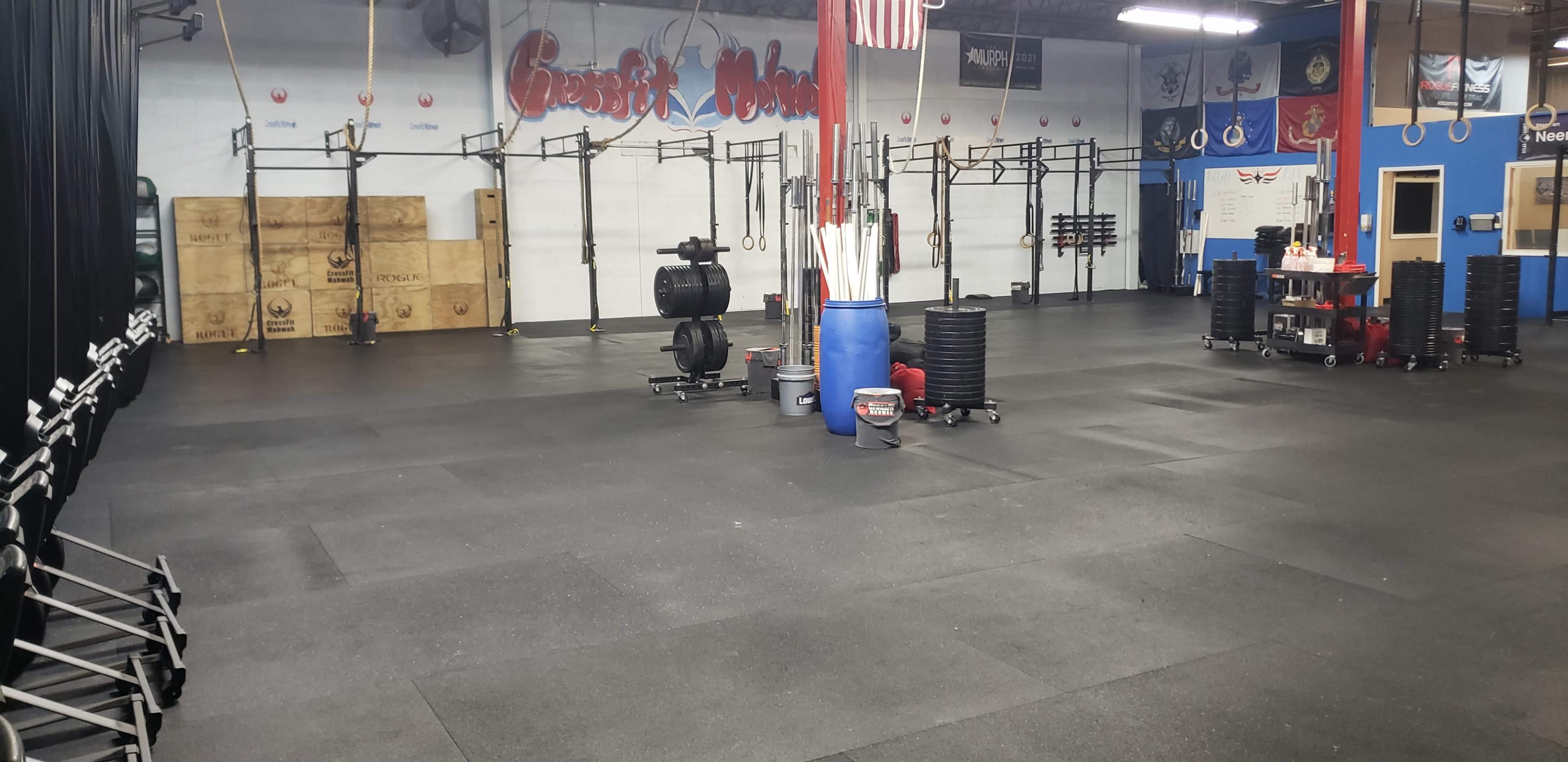 The interior of a gym with workout equipment, including weights and squat racks, arranged in an organized space with rubber flooring.