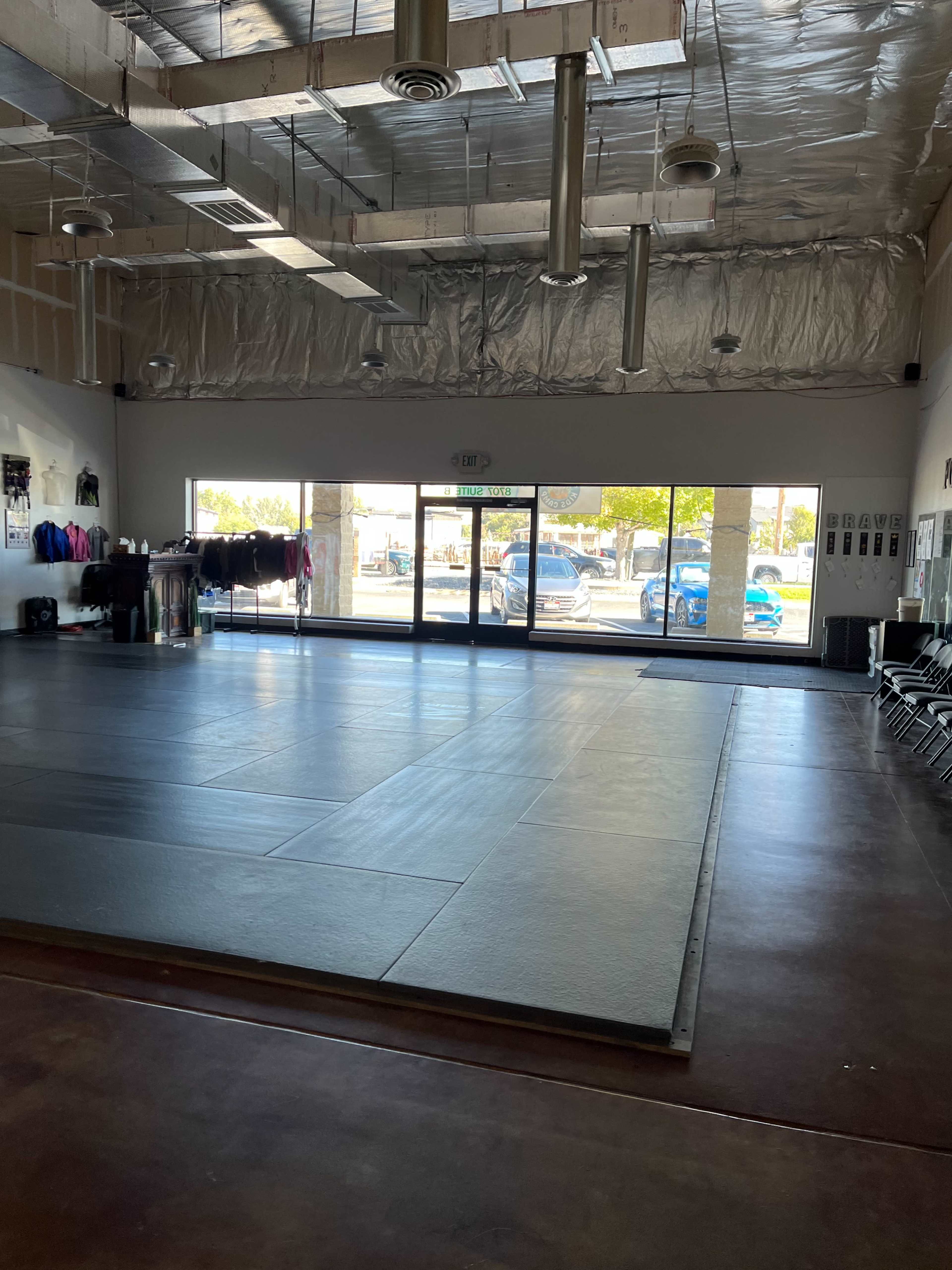 The image shows a spacious martial arts studio with a large, empty mat area and windows that provide a view of the outside.