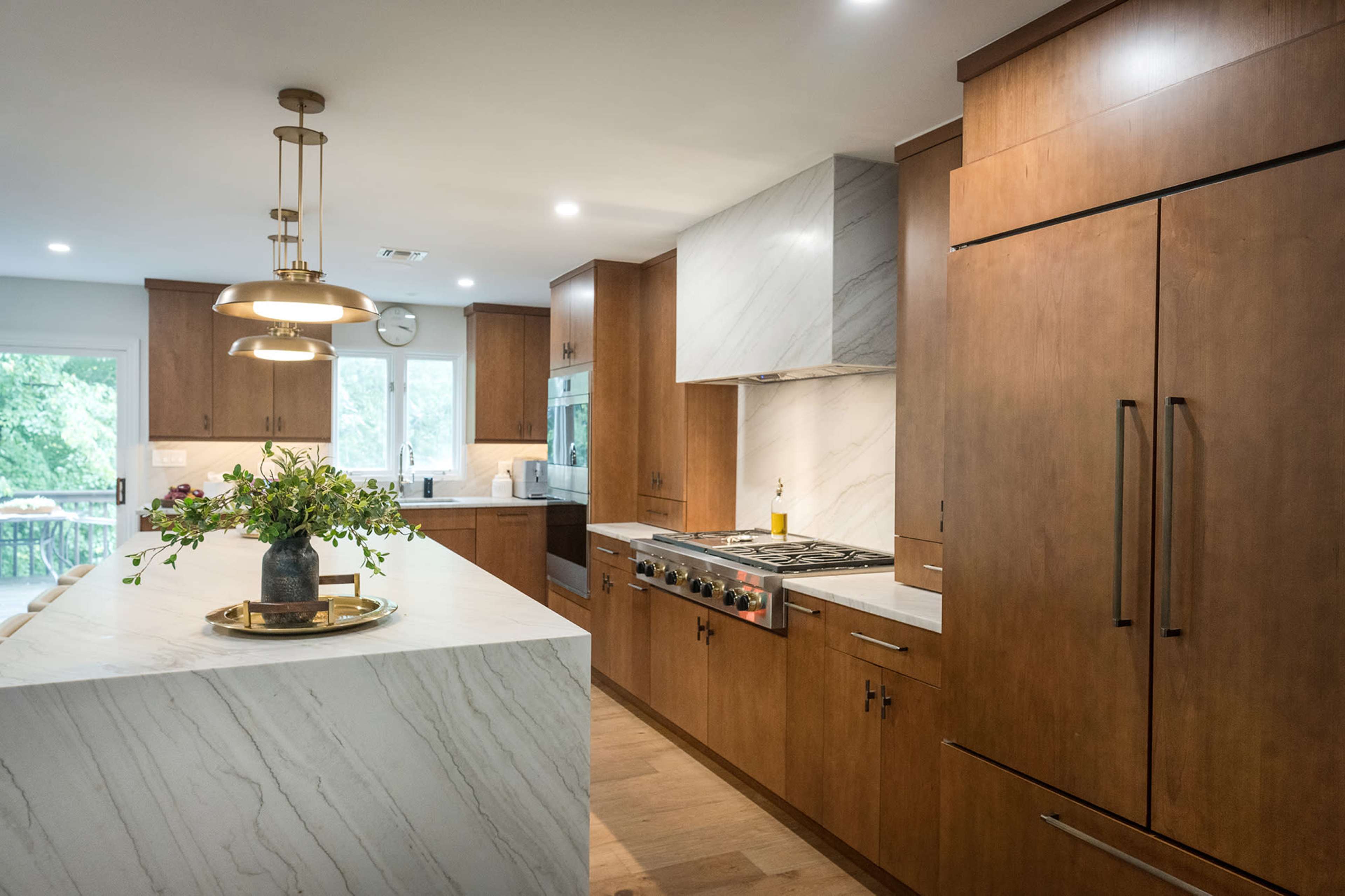 The kitchen features wooden cabinets, a marble countertop, and modern appliances, with a large island at its center.