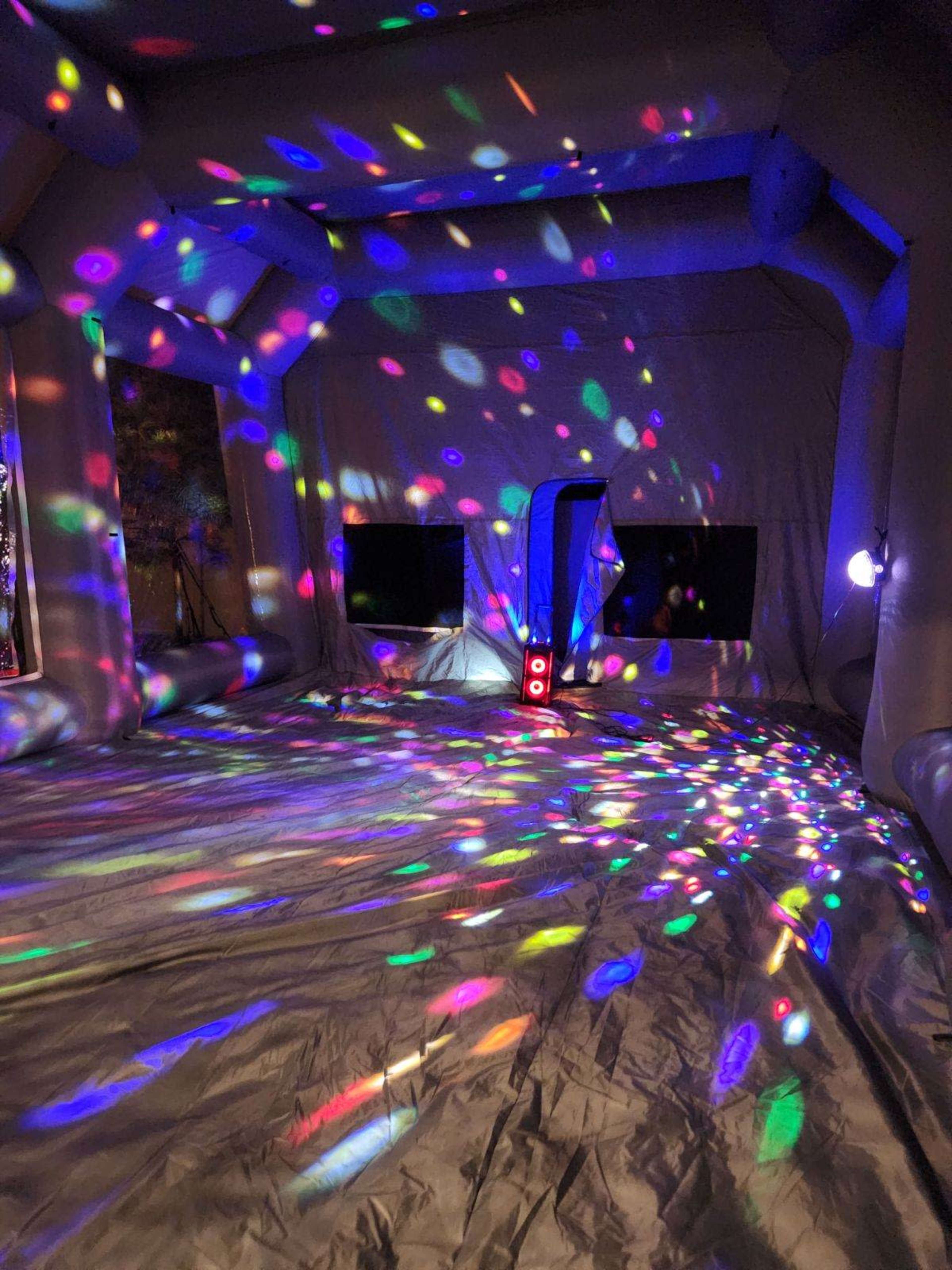The interior of an inflatable structure is illuminated with colorful, circular lights on the floor and walls.