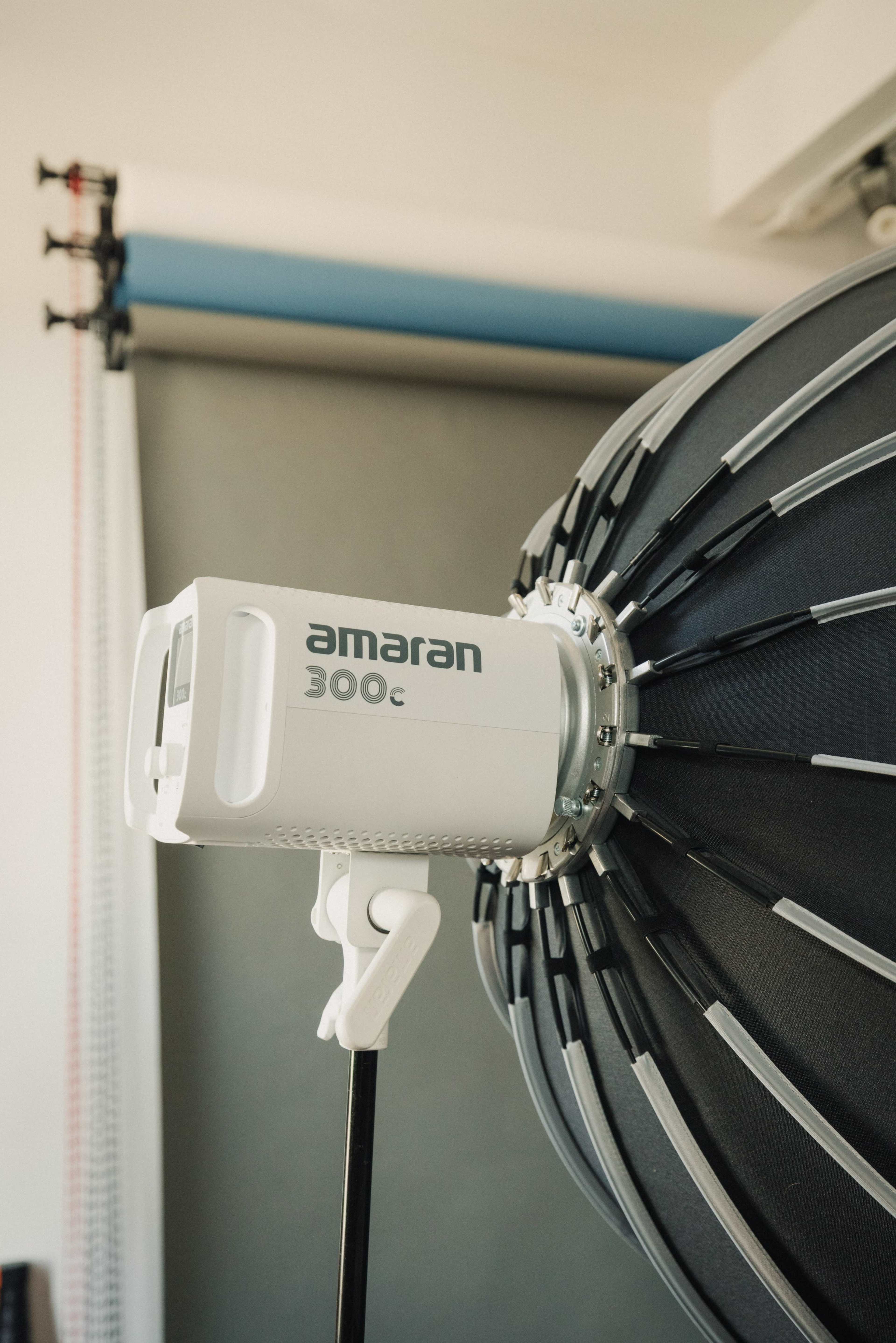 The image shows a lighting setup featuring an Amaran 300C light attached to a large softbox in a photography studio.