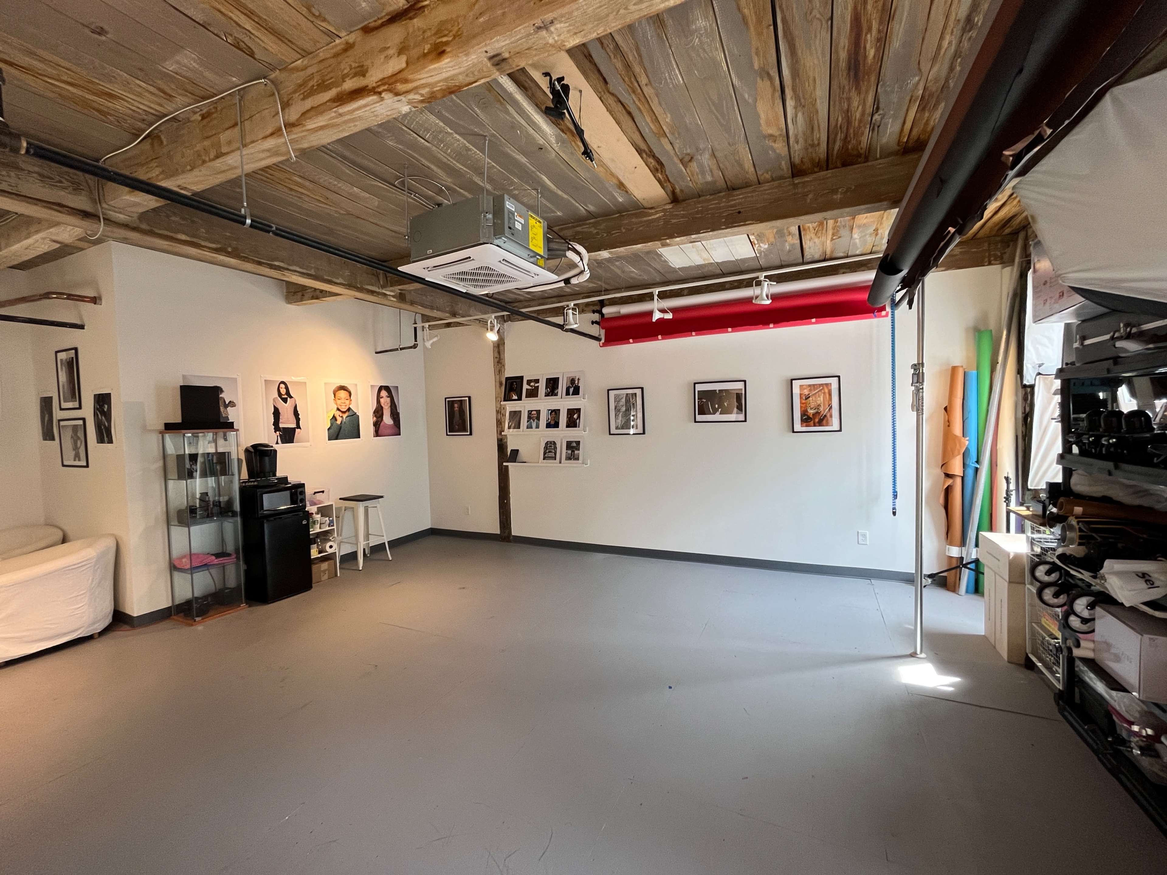 A spacious room with exposed wooden beams, featuring various framed photographs on the walls, a couch, and storage shelves on one side.