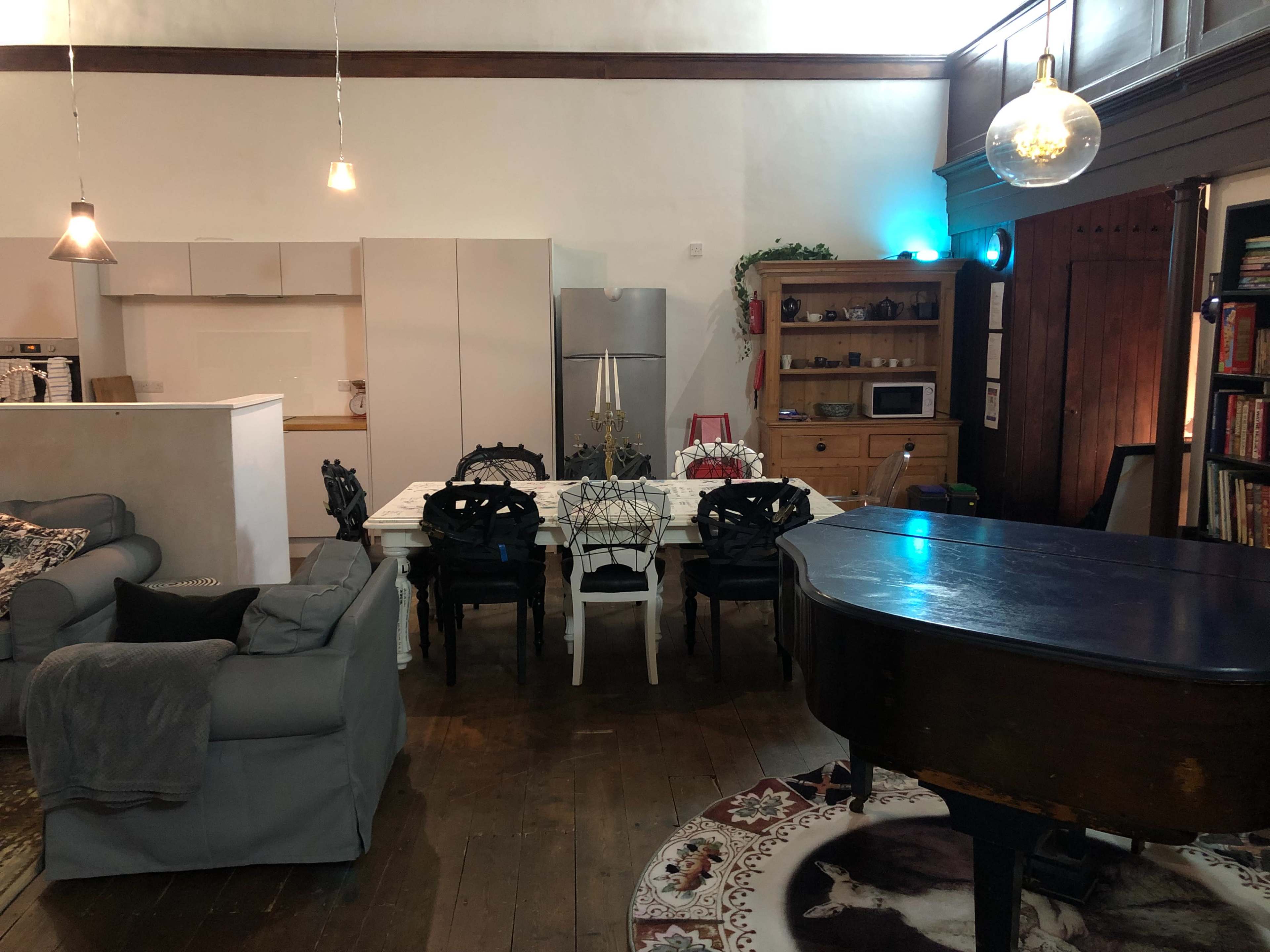 A spacious interior with a dining table surrounded by chairs, a grand piano, and a combination of modern and wooden furniture.