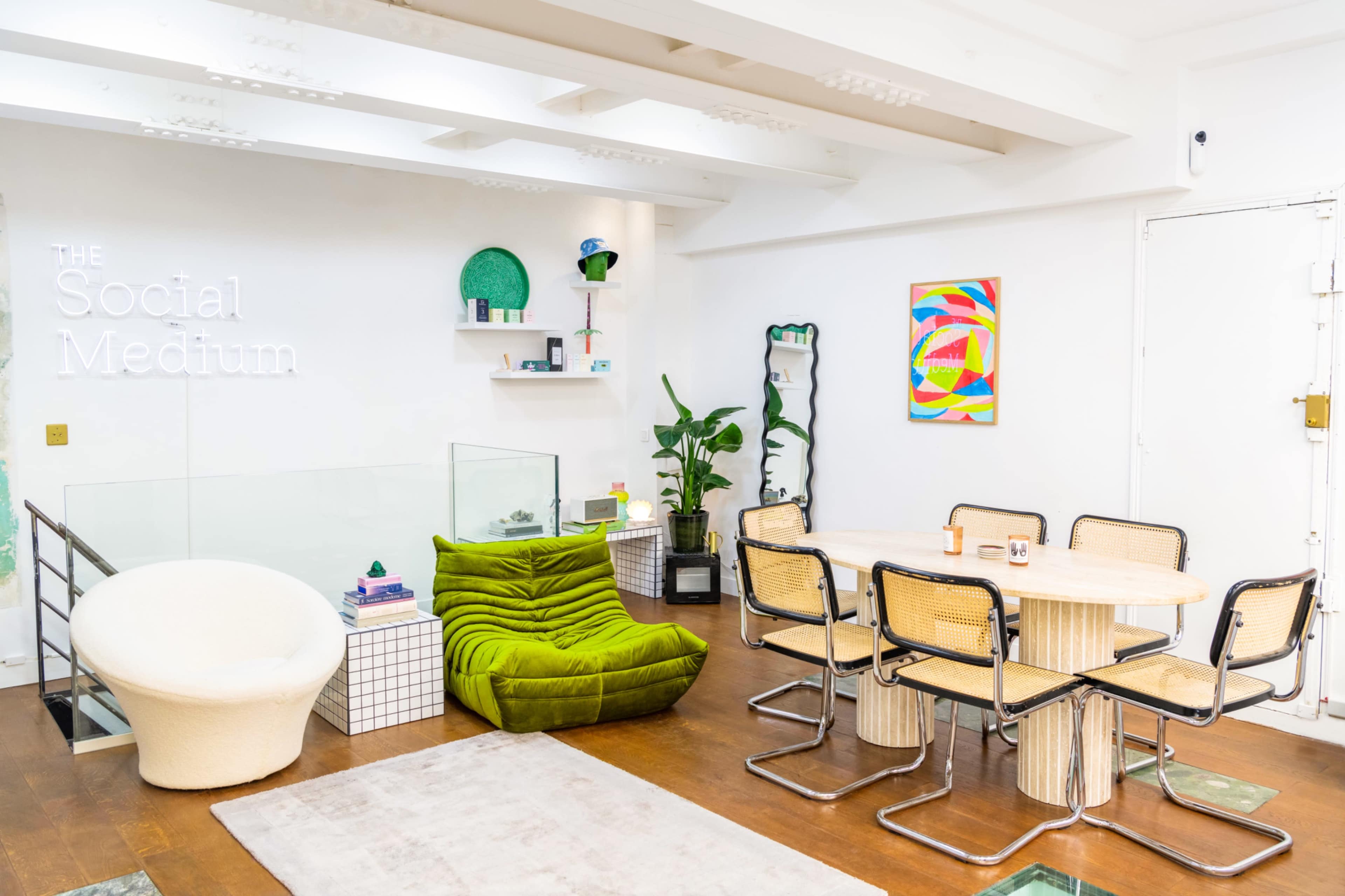 A modern interior features a dining area with a round table and chairs, a green couch, and decorative elements including plants and artwork.