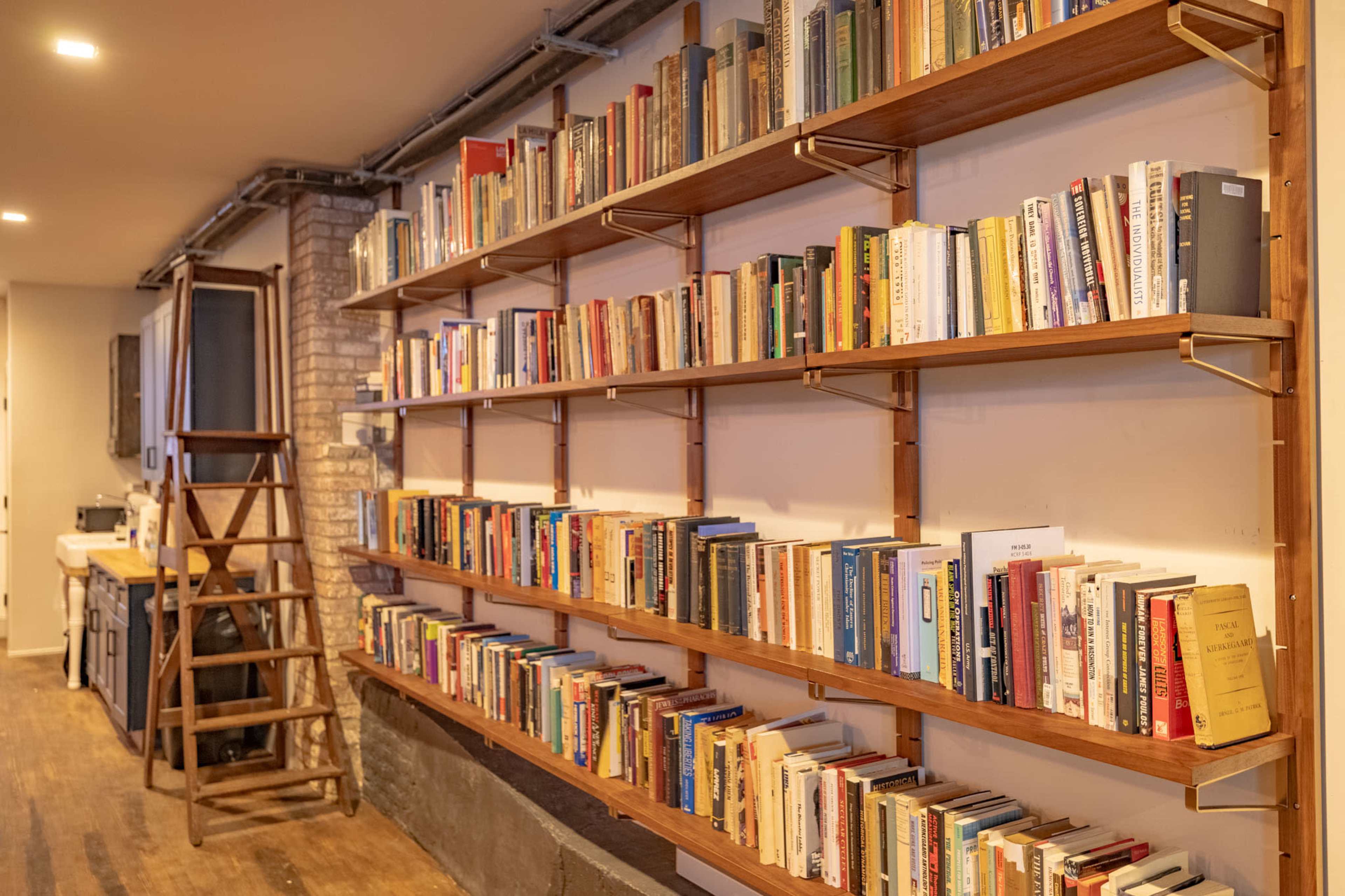 A wall-mounted bookshelf filled with various books, accompanied by a wooden ladder positioned nearby.