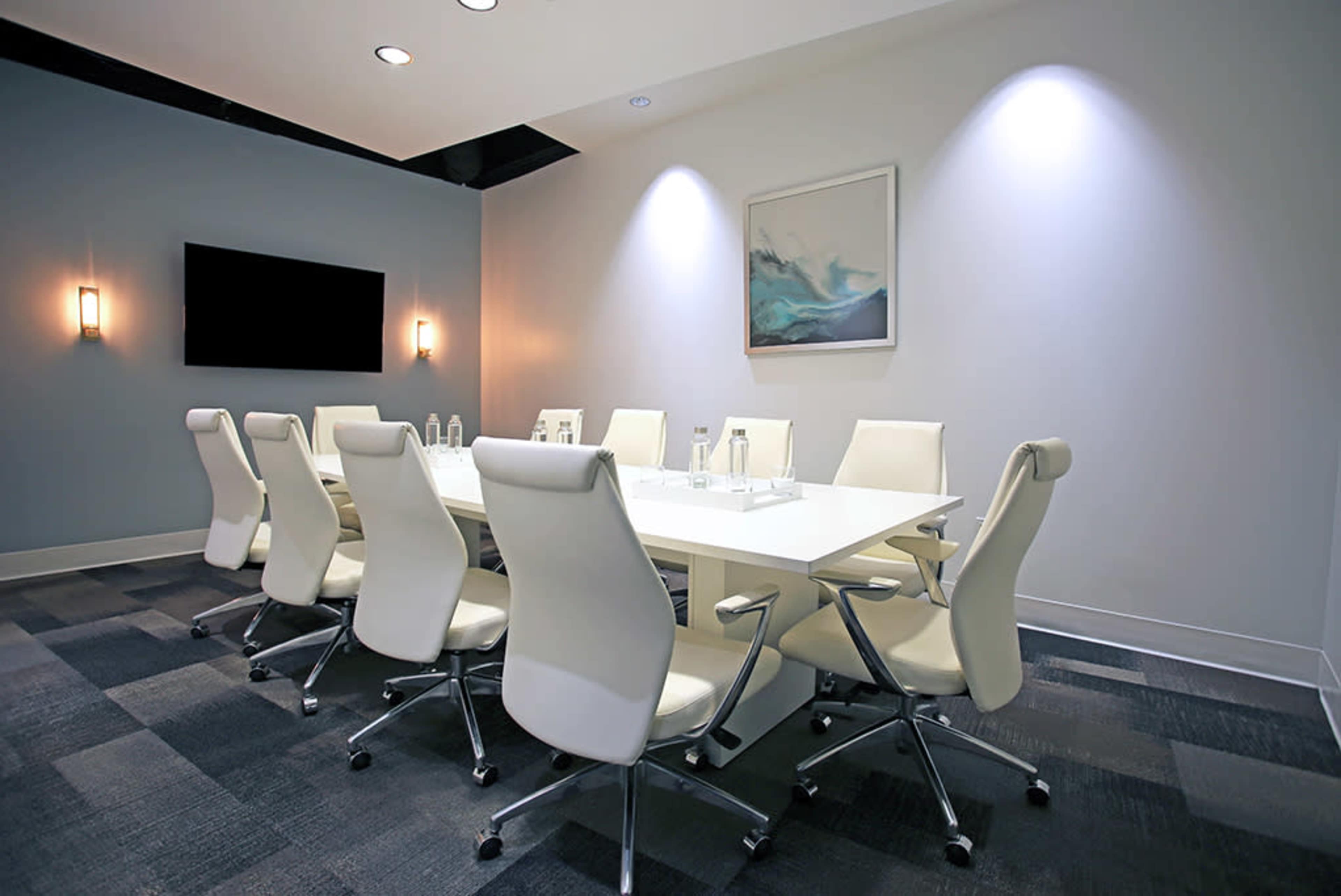A modern conference room with a long white table surrounded by white ergonomic chairs, illuminated by soft wall-mounted lights.