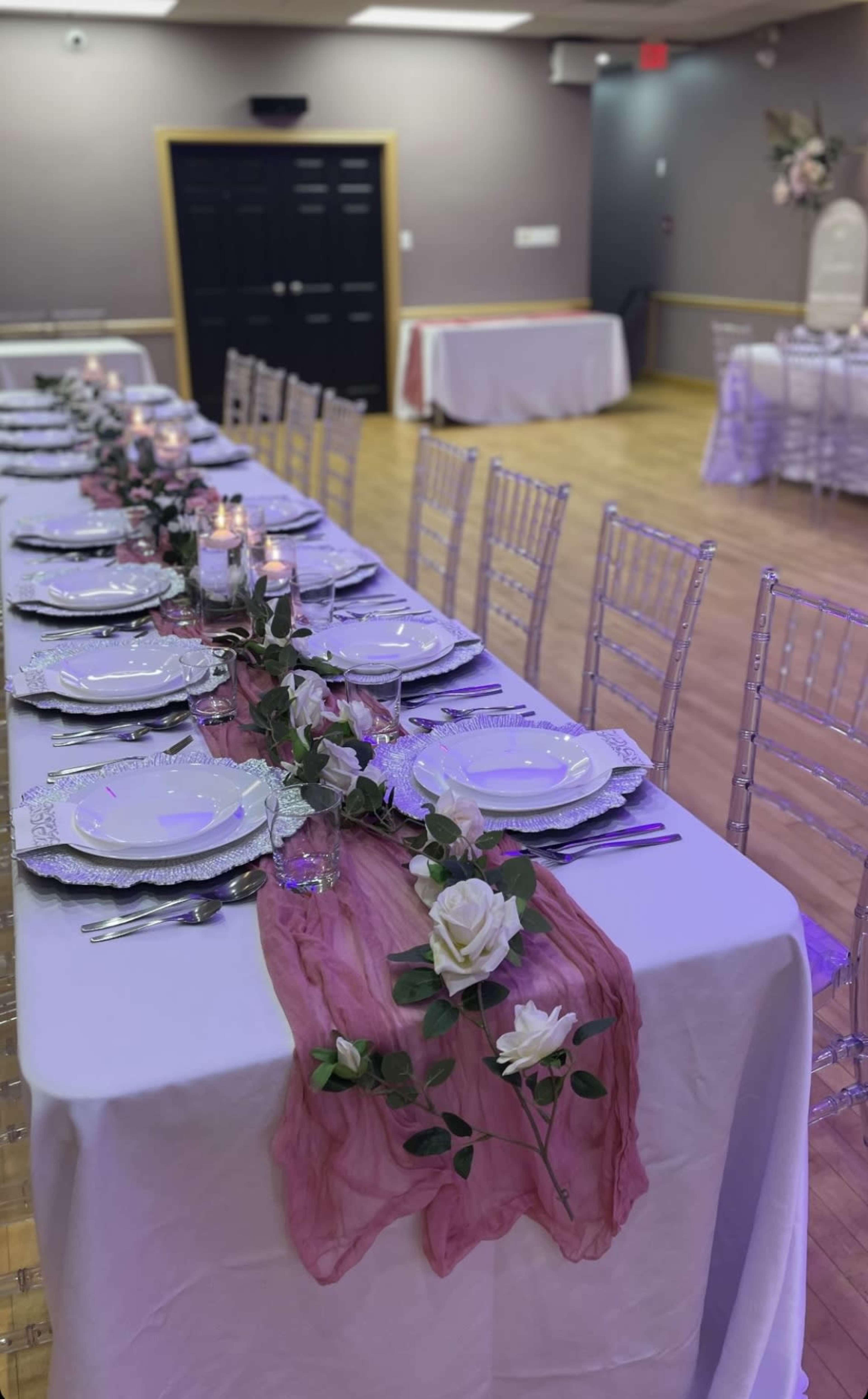 A long table is elegantly set with white plates and glasses, adorned with a floral centerpiece and a pink runner in a banquet hall.