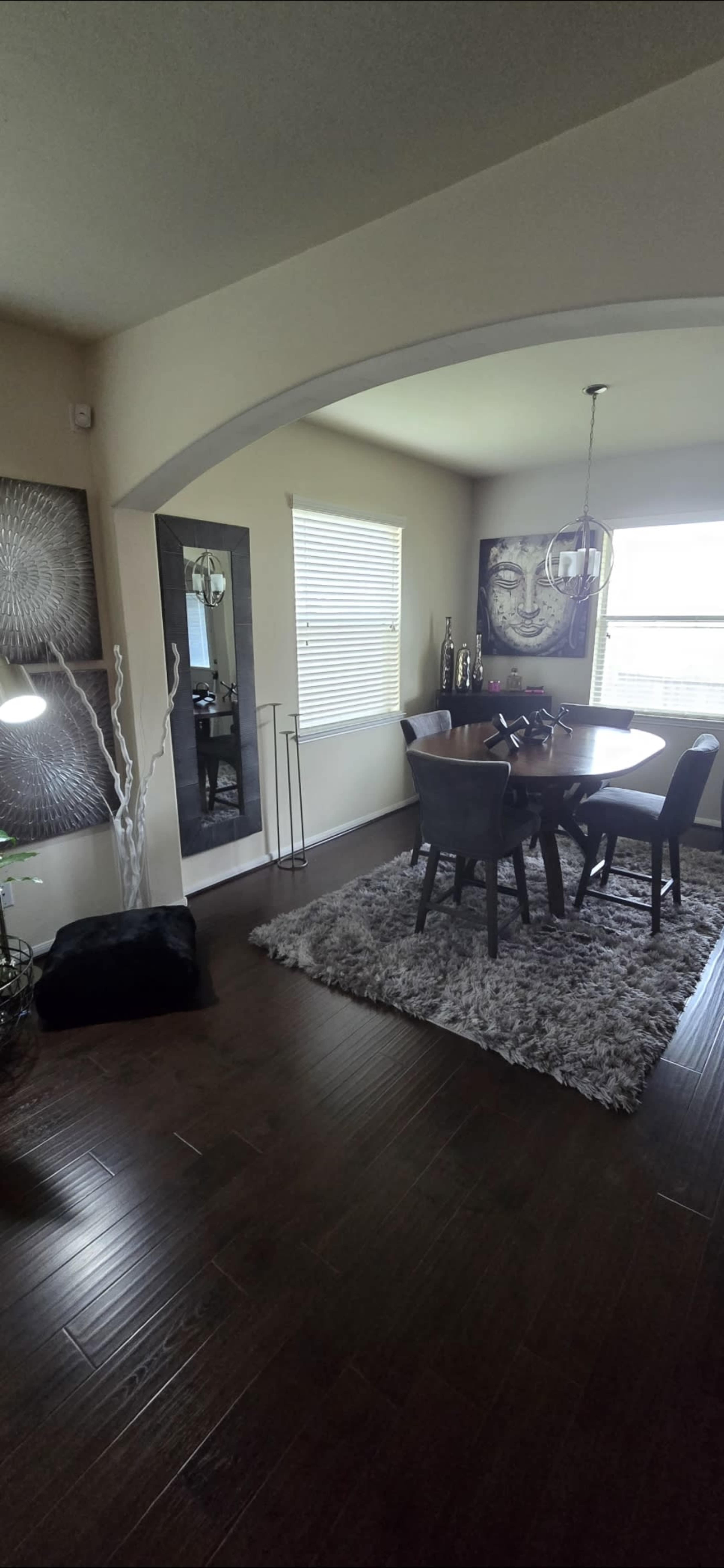 A dining area features a round table with chairs, surrounded by wall decor, a rug, and natural light from a window.