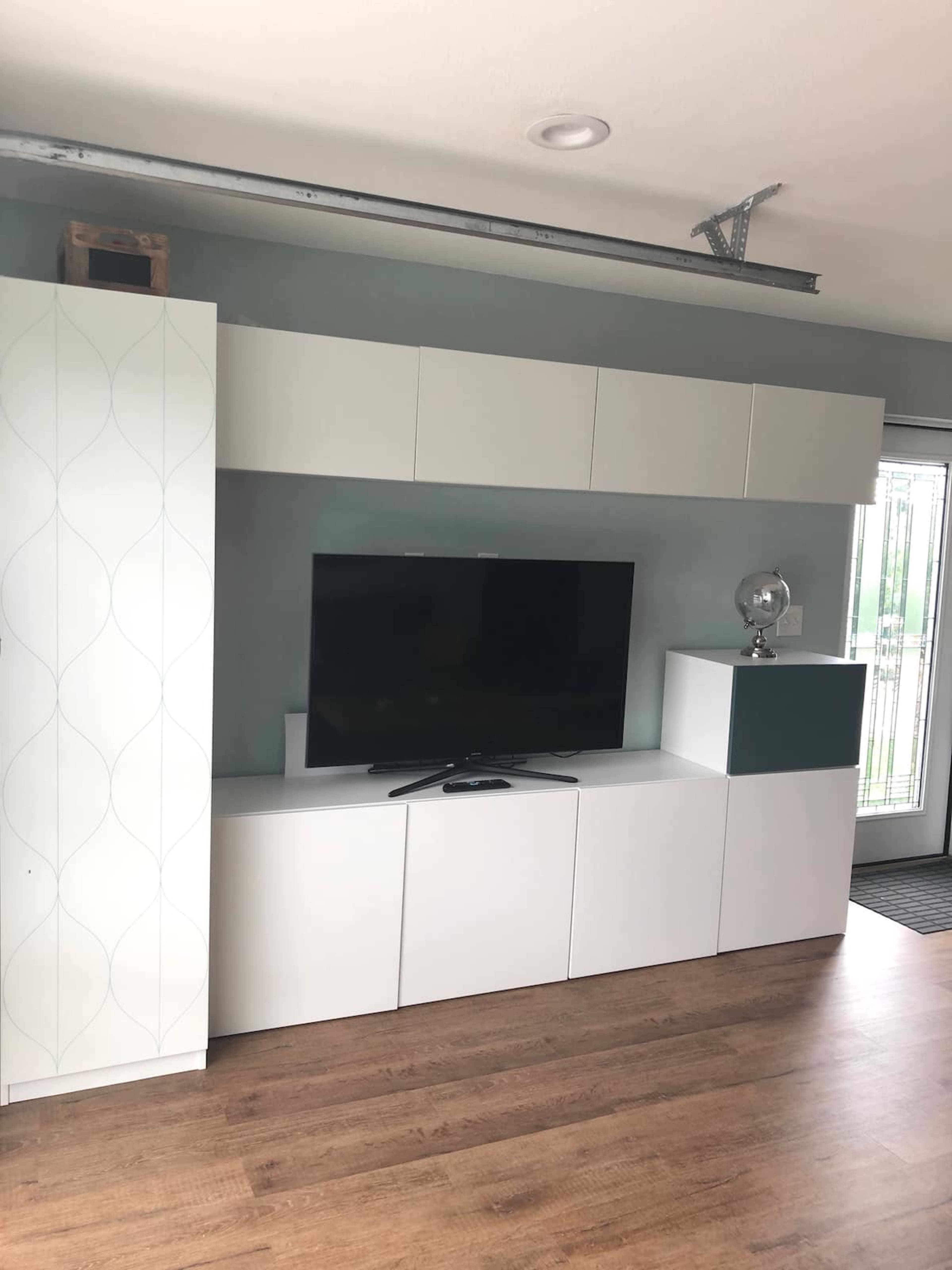 A modern living room setup with a wall-mounted television and white cabinetry against a light green wall.