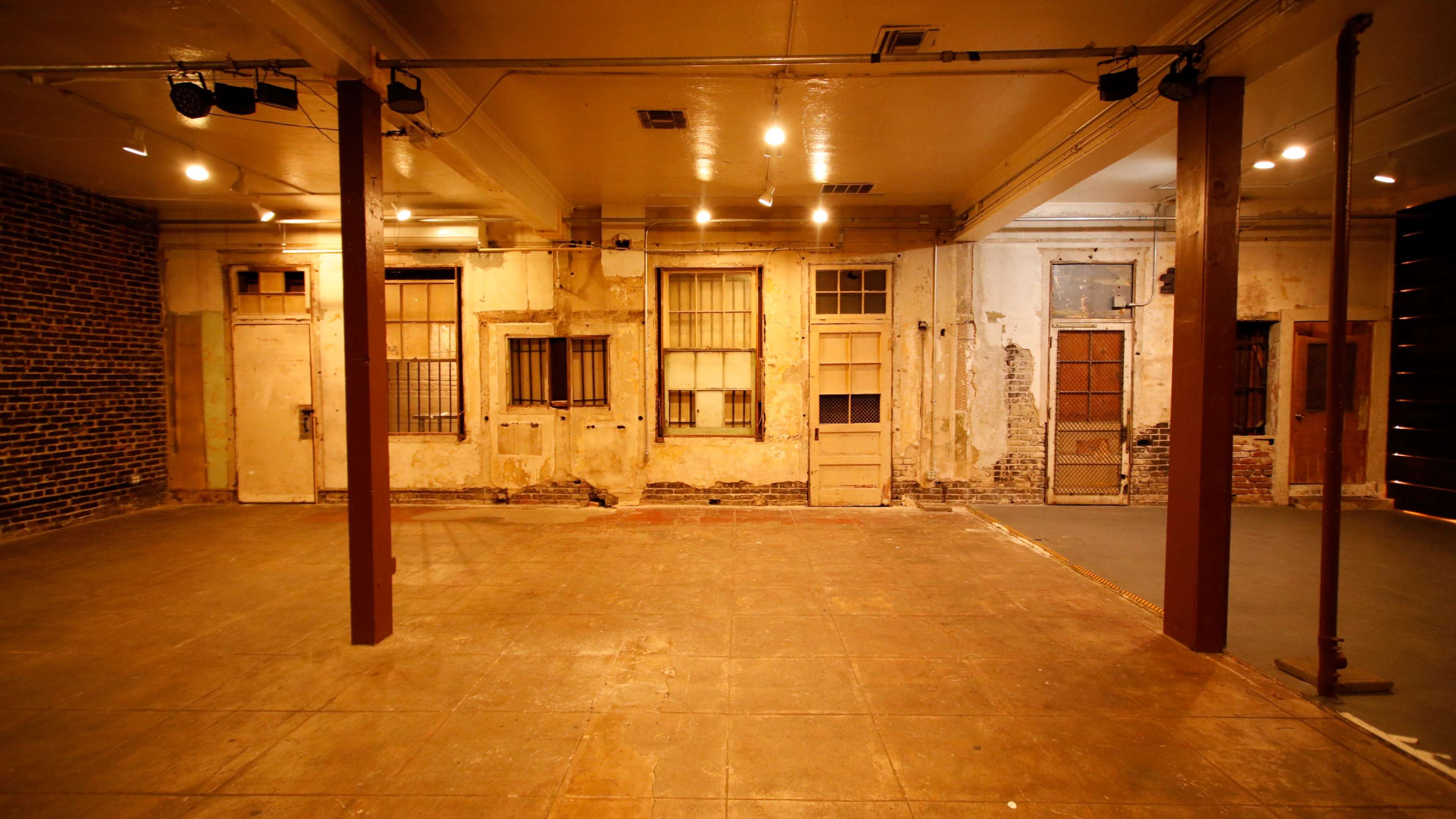 An empty, weathered room with exposed brick walls and several doors along one side.