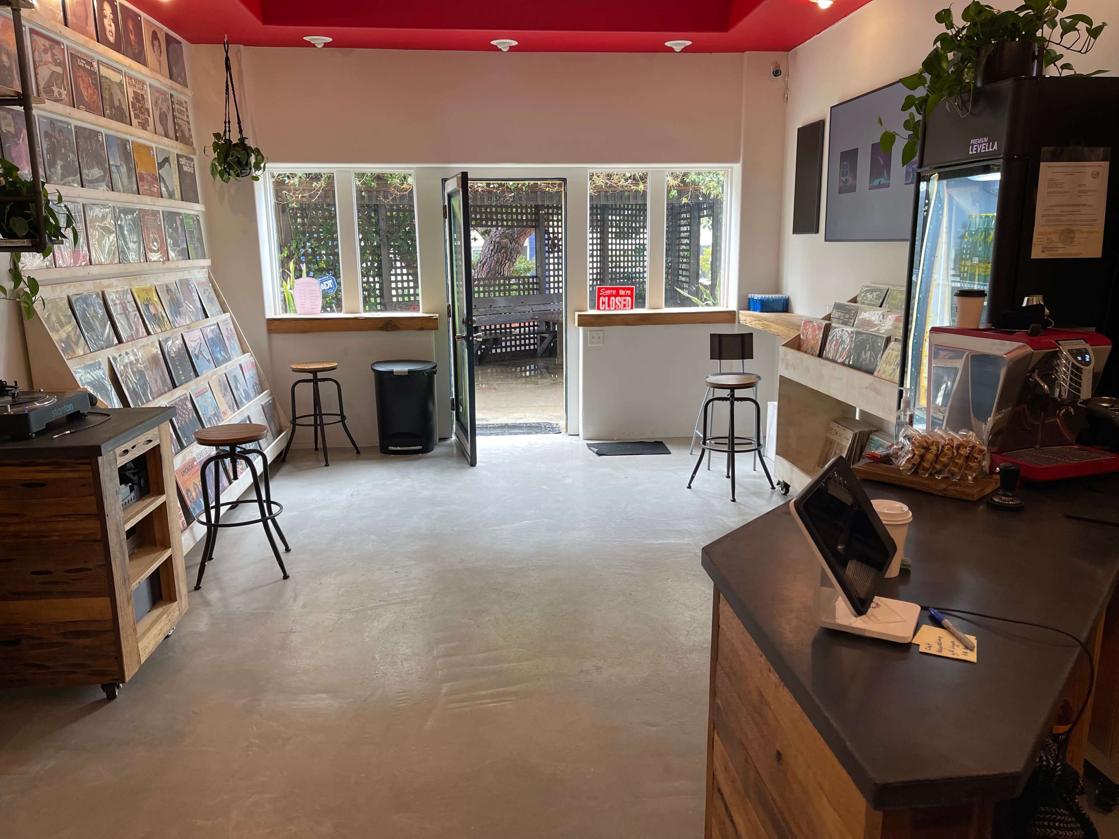 An interior of a cafe with walls lined with vinyl records, a couple of bar stools, and an open door leading outside.