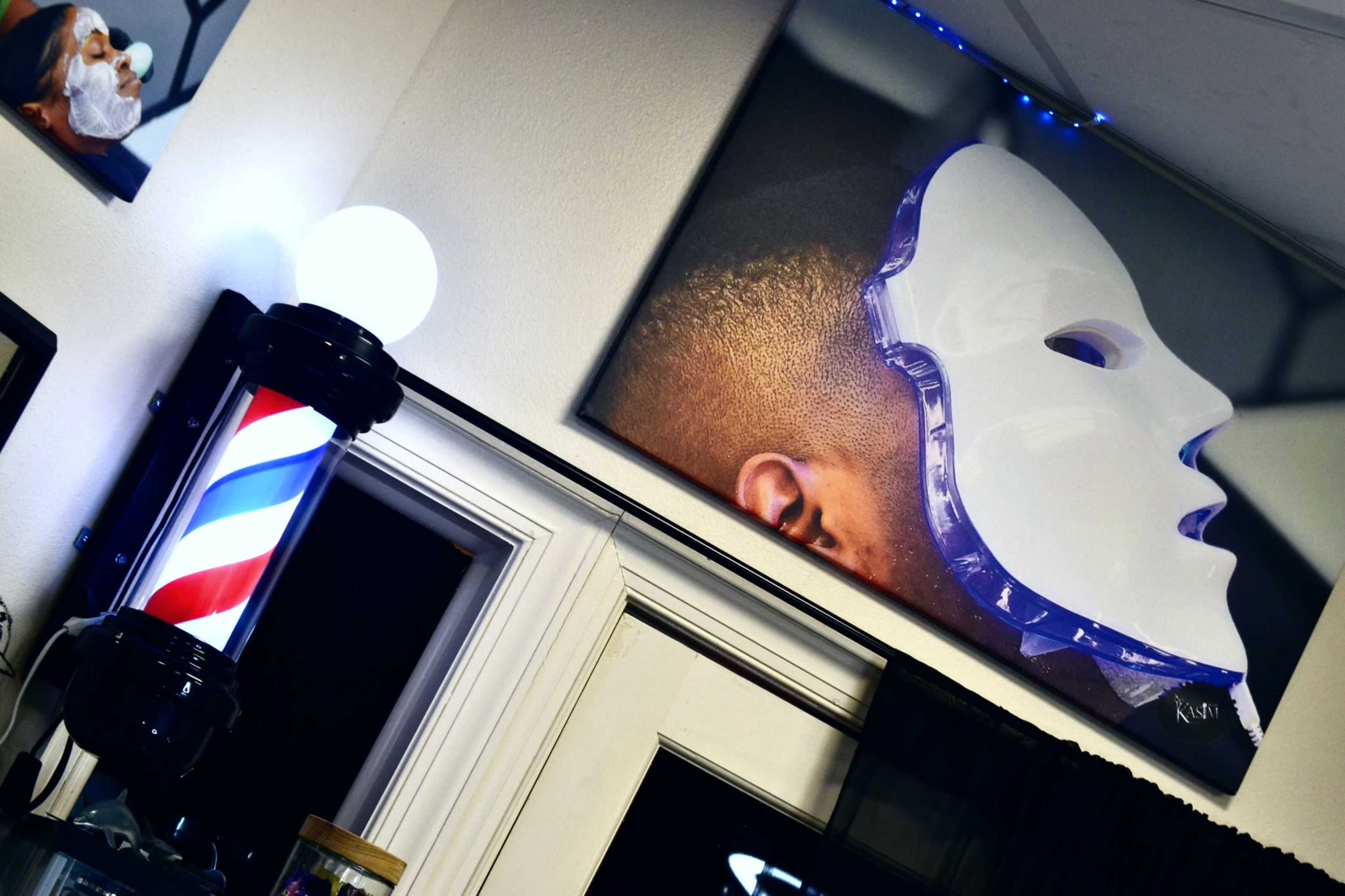 A barber pole next to a large portrait of a person wearing a white mask, displayed on the wall of a barbershop.