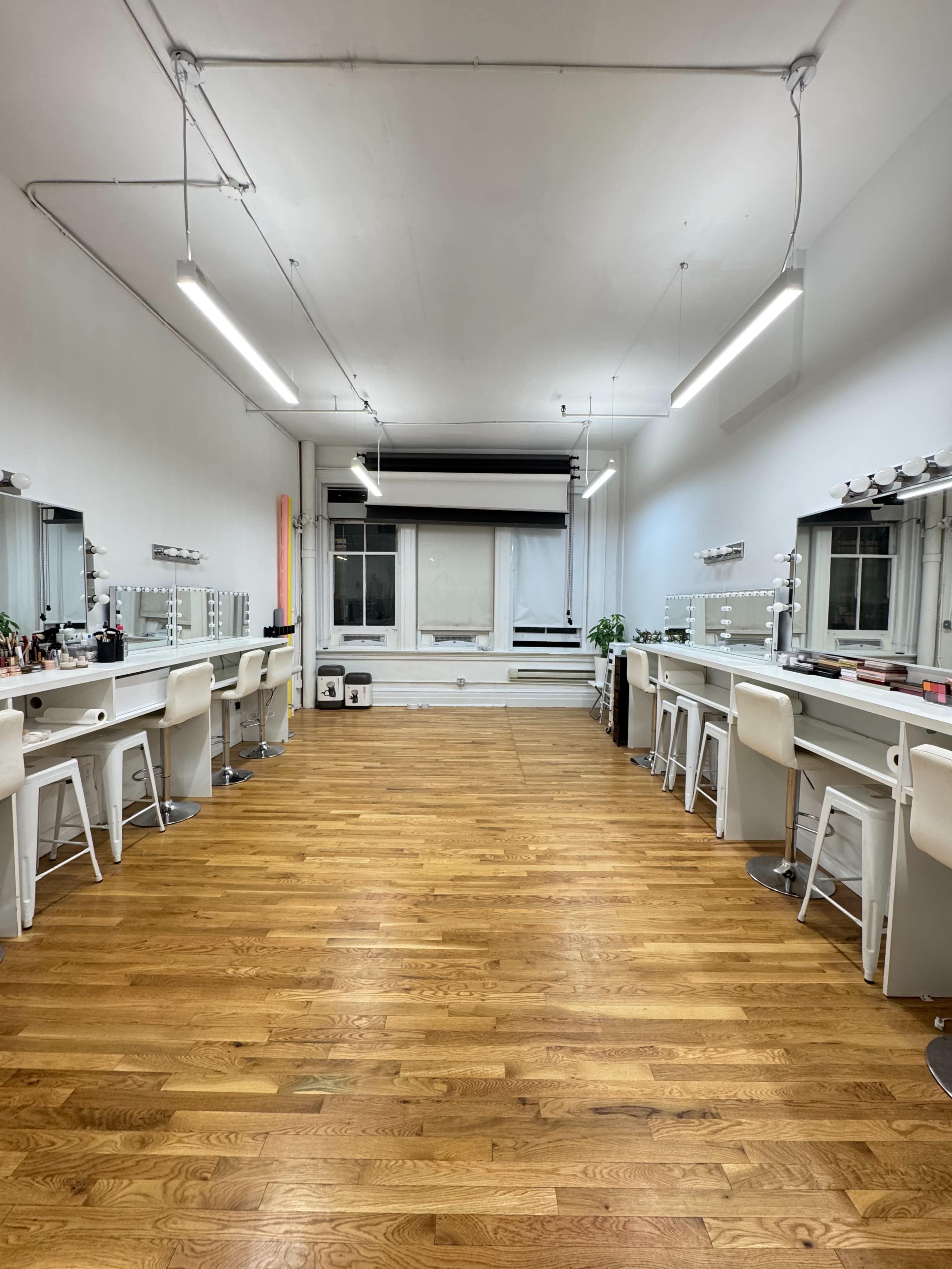 The image shows a well-lit vanity room with multiple makeup stations and wooden flooring.