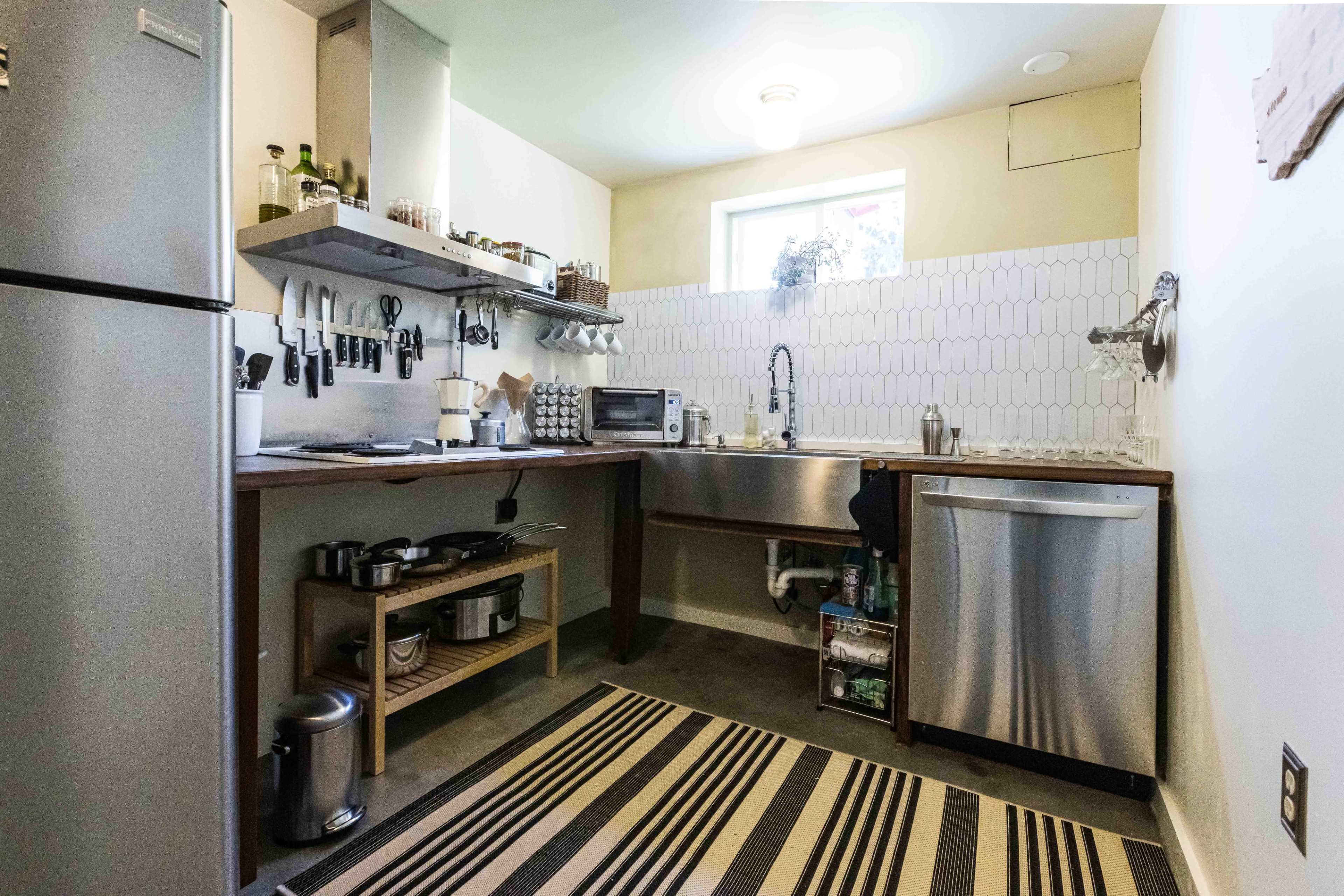 The image shows a modern kitchen equipped with stainless steel appliances, wooden countertops, and a variety of kitchen utensils organized on the wall.