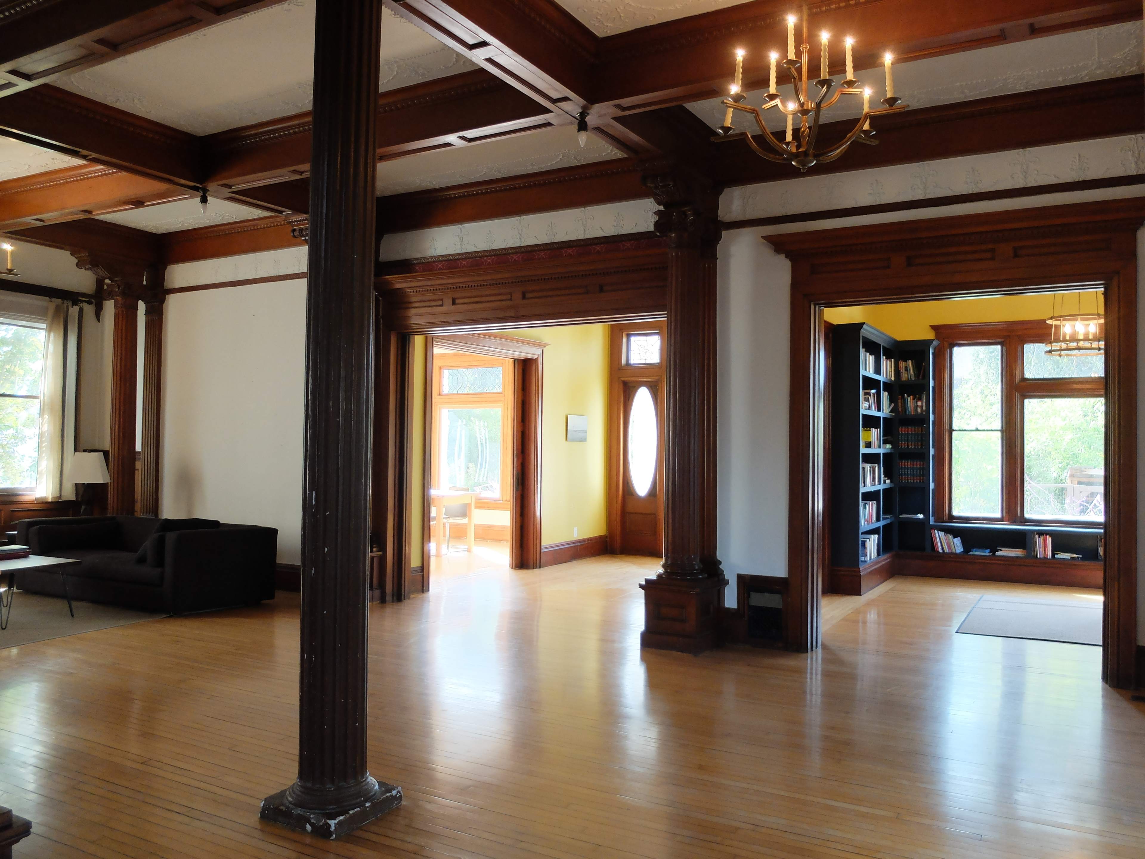 A spacious room with wooden flooring, large windows, and architectural elements including columns and crown molding.