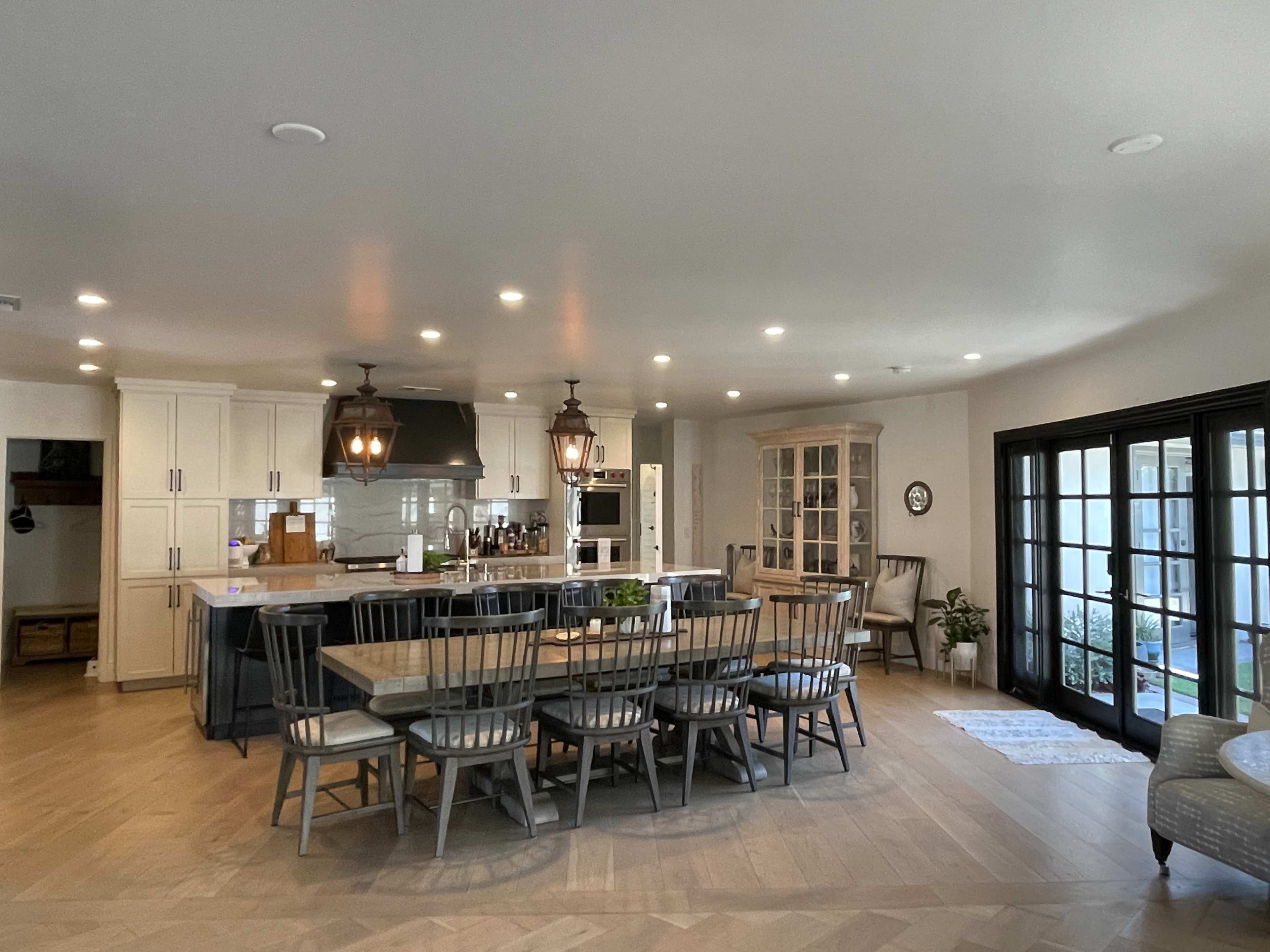 A modern kitchen with an island, dining table, and a combination of light and dark cabinetry, adjacent to a living area with large windows.