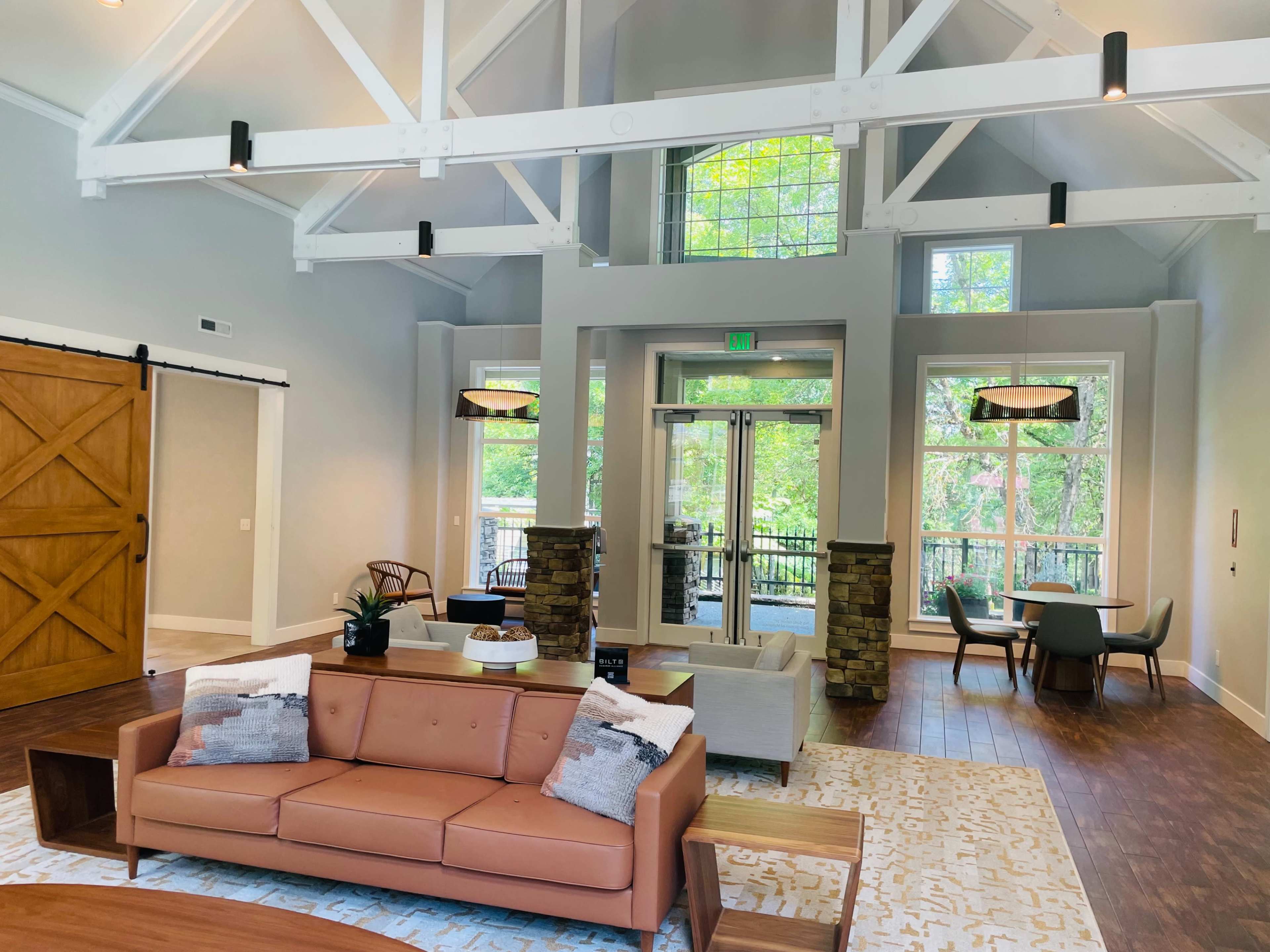 A modern, well-lit living area with a brown leather sofa, large windows, and a mix of seating options, including a dining table and chairs.