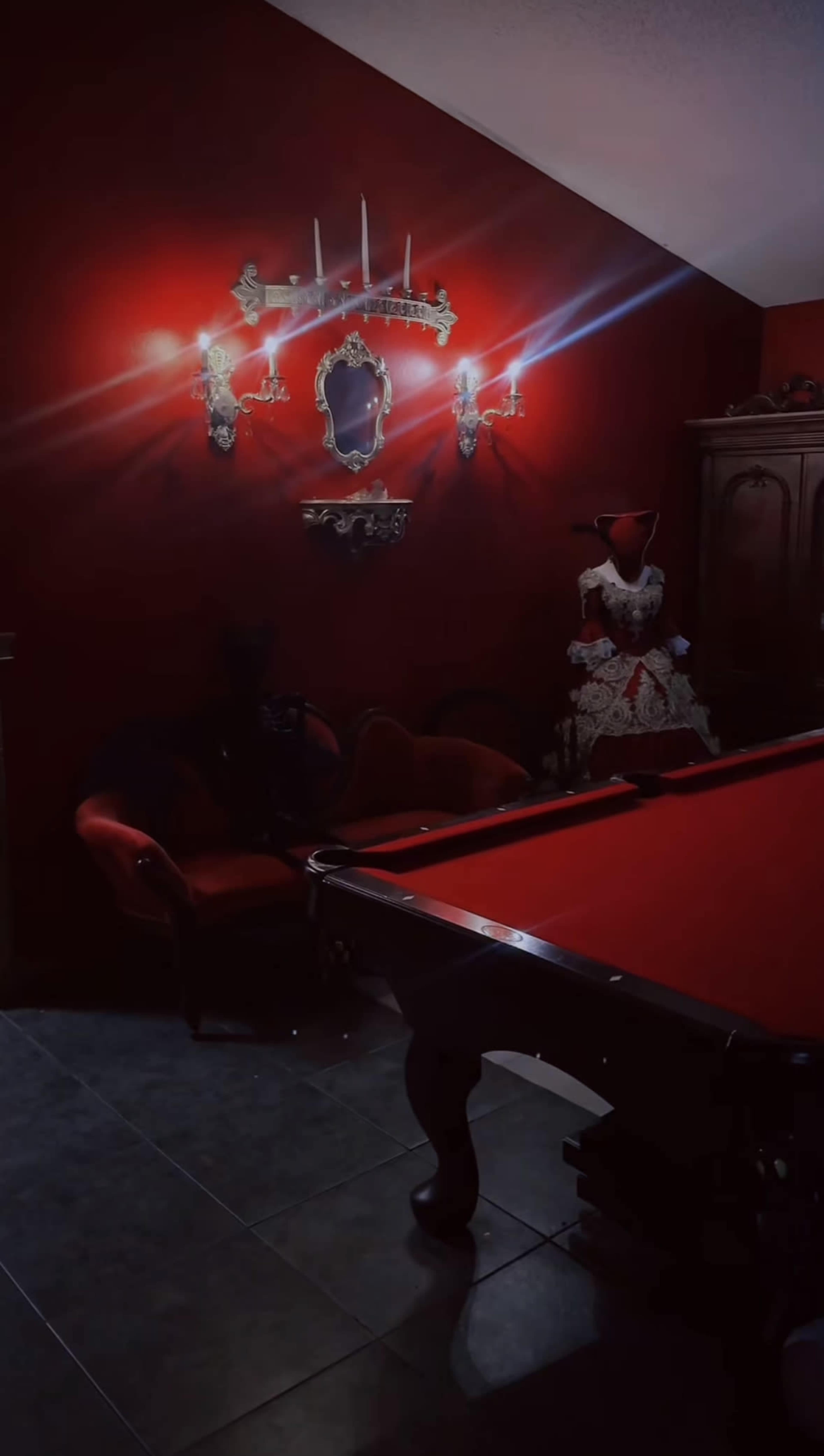 The room features a red wall, a billiard table, a vintage mirror, and a mannequin dressed in a white gown.