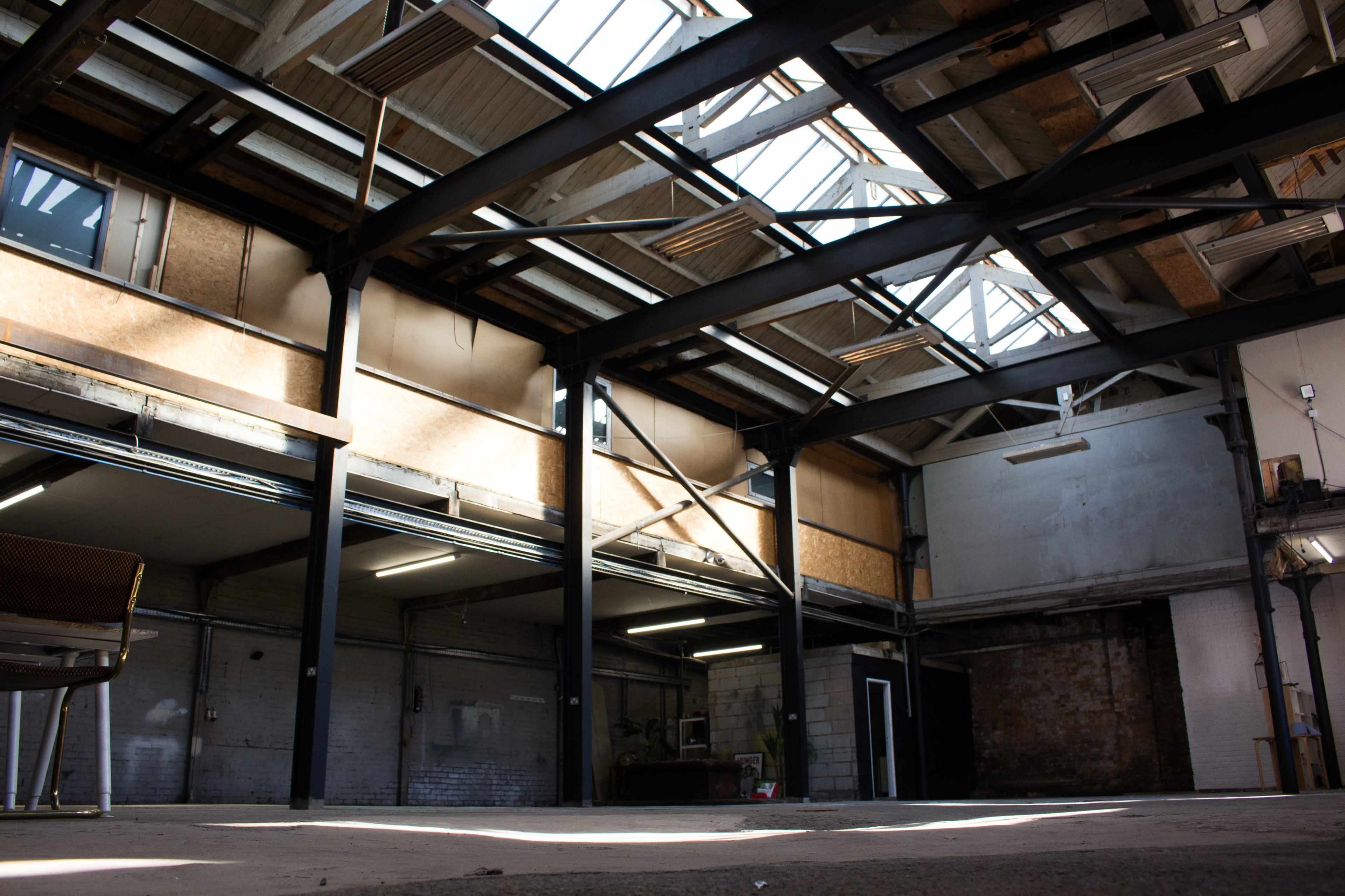 The interior of a spacious industrial warehouse with large windows allowing natural light to enter.