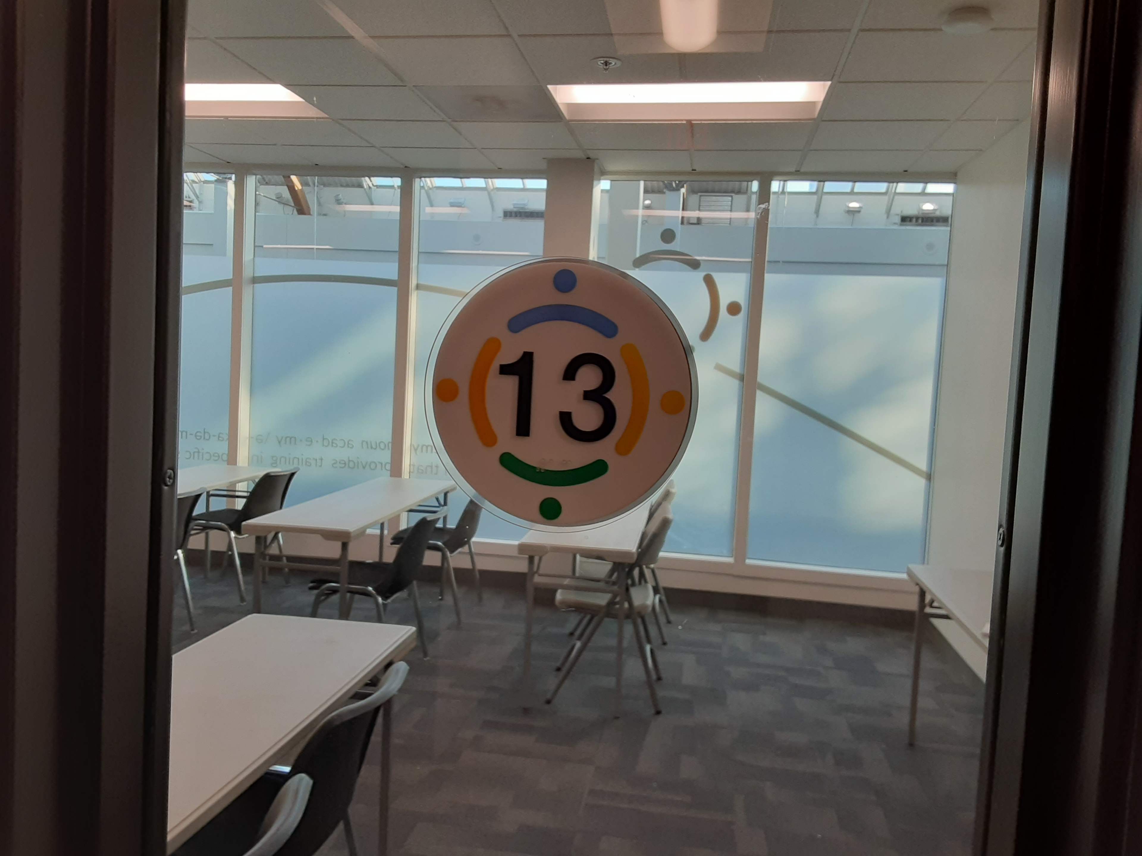 A classroom door with a round sign displaying the number "13" and colorful dots.