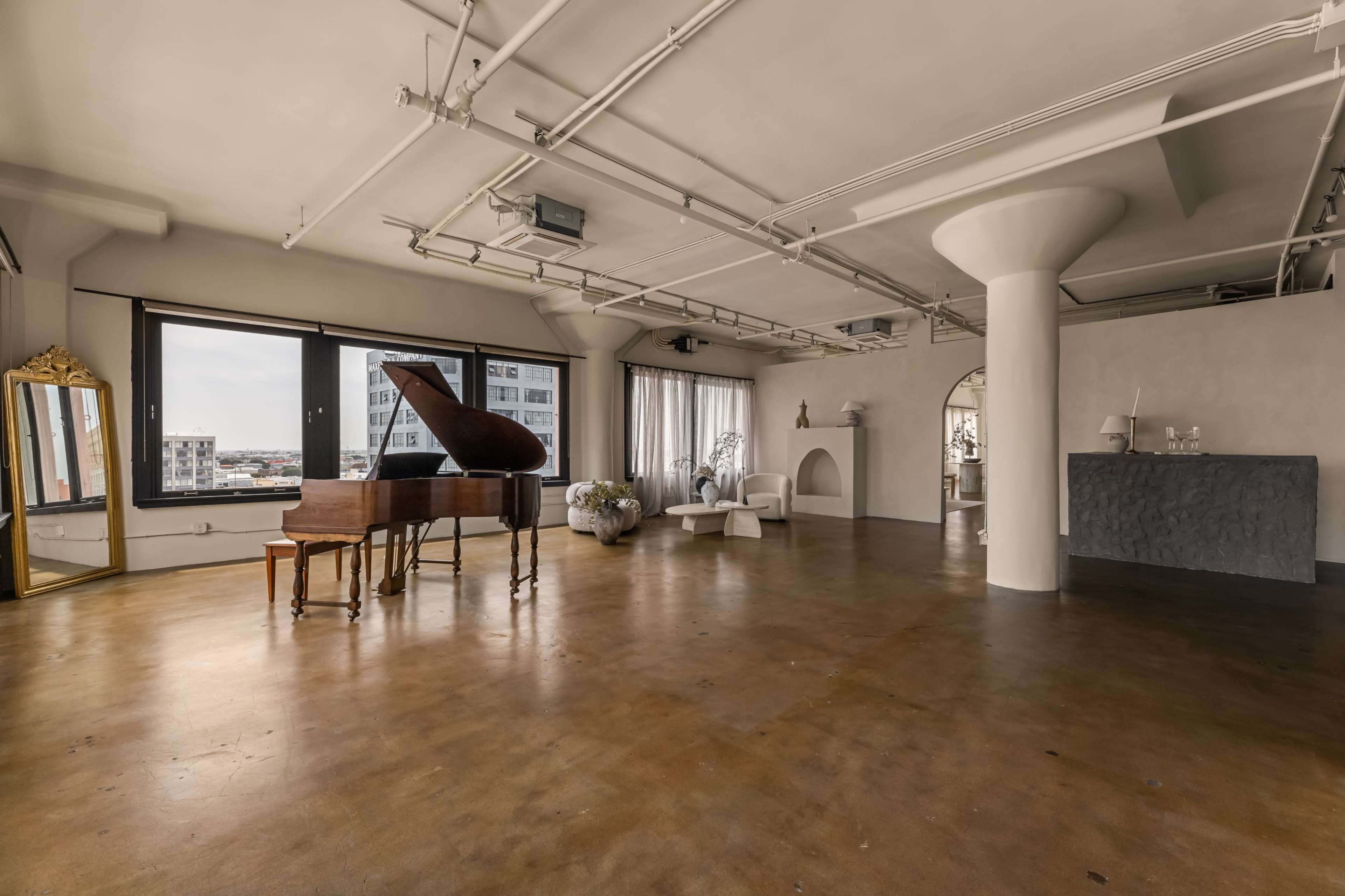 The image shows a spacious, modern interior with a grand piano, minimalist furniture, and large windows offering a view of the city.