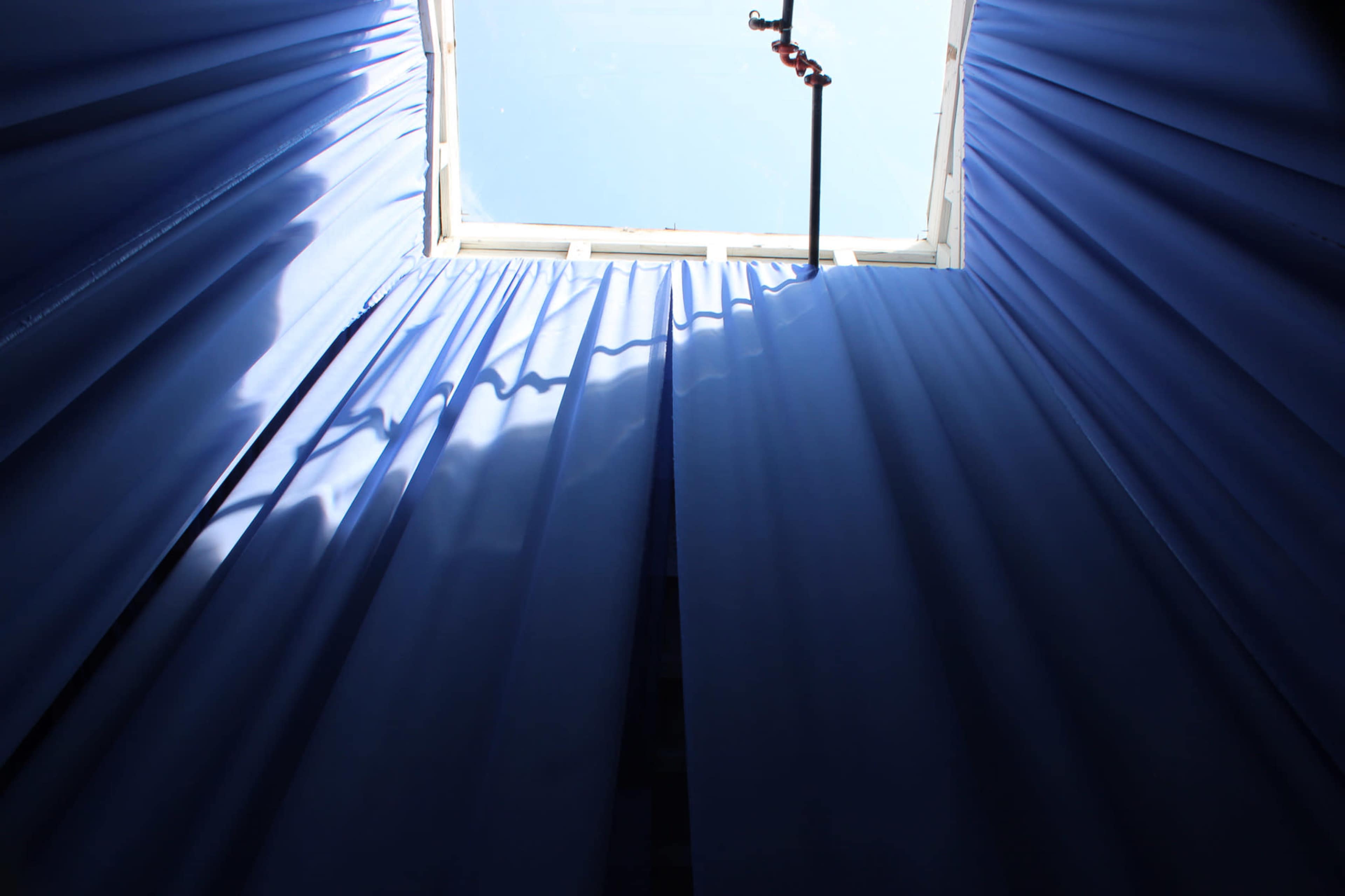 A view looking up at a bright sky through a window framed by blue curtains.