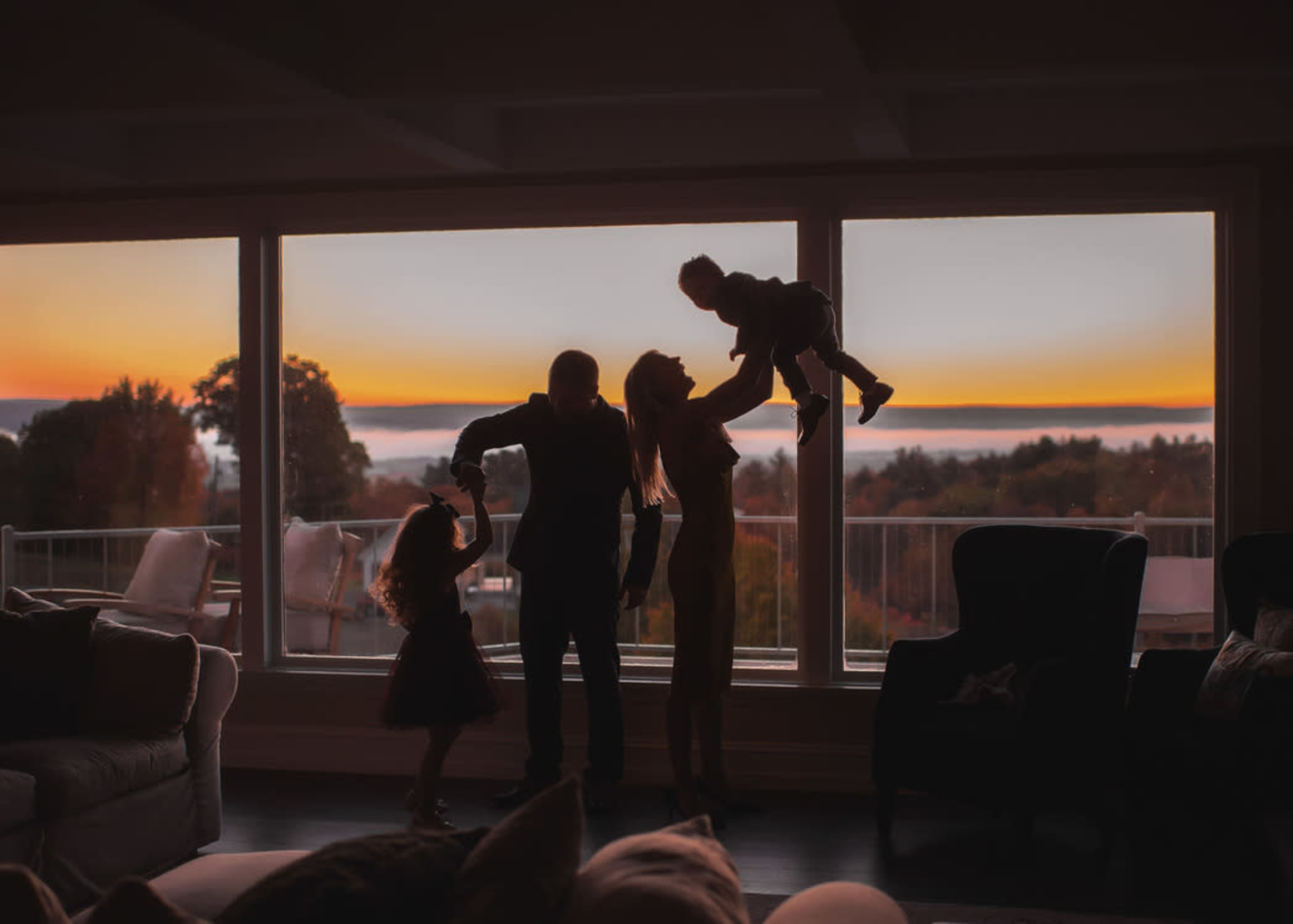 A family of four is silhouetted against a sunset seen through large windows.