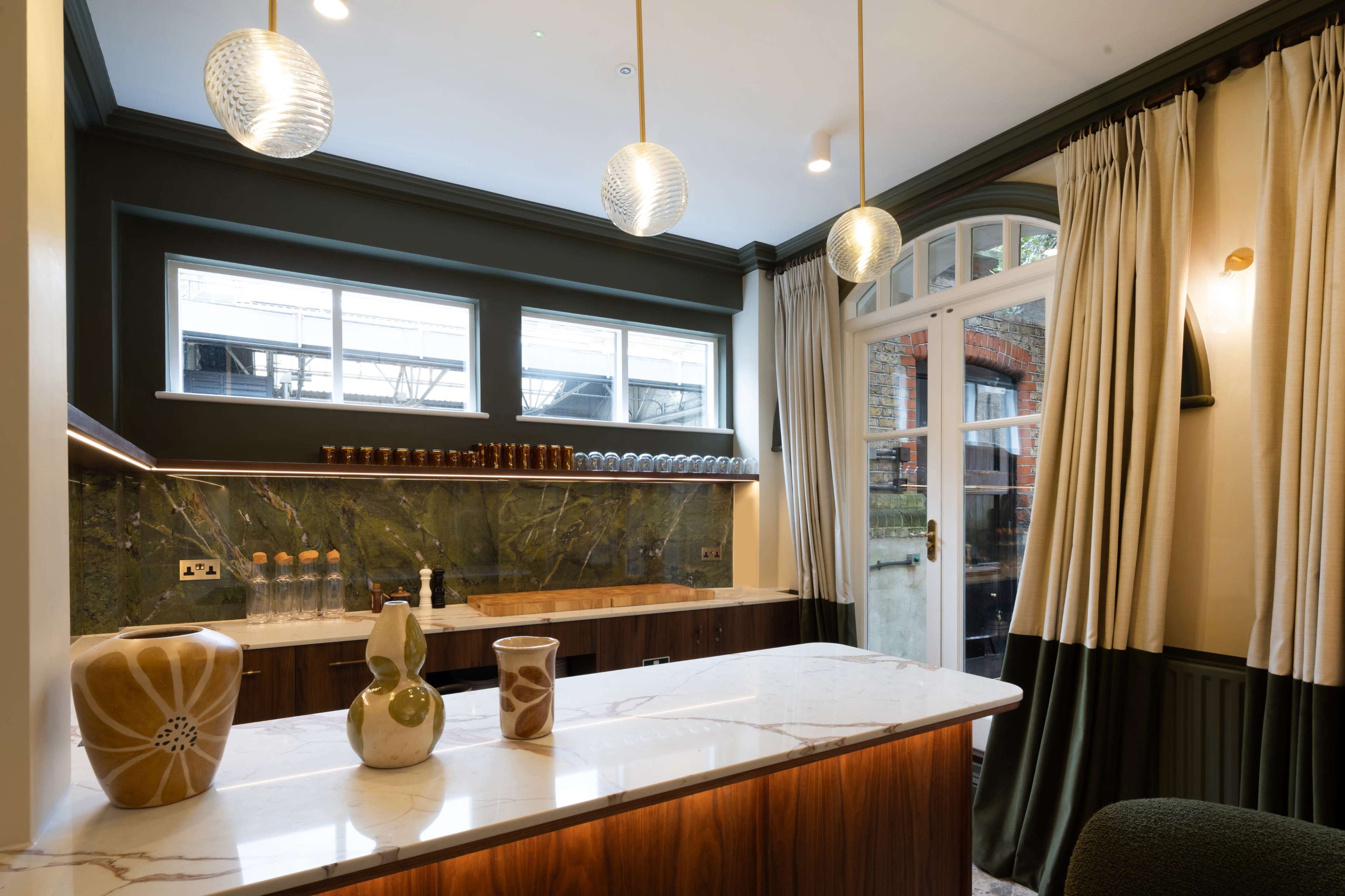 The image shows a modern kitchen featuring a marble countertop, decorative vases, and large windows with light cream curtains.