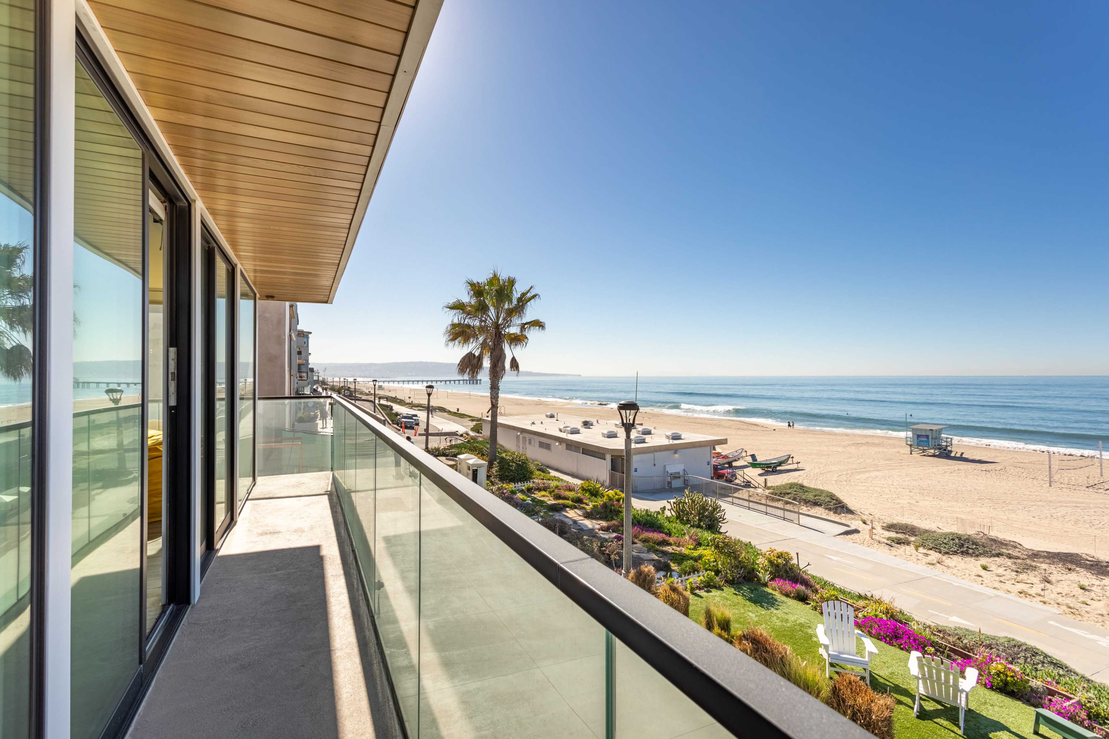 A balcony overlooks a sandy beach with palm trees and a clear sky.