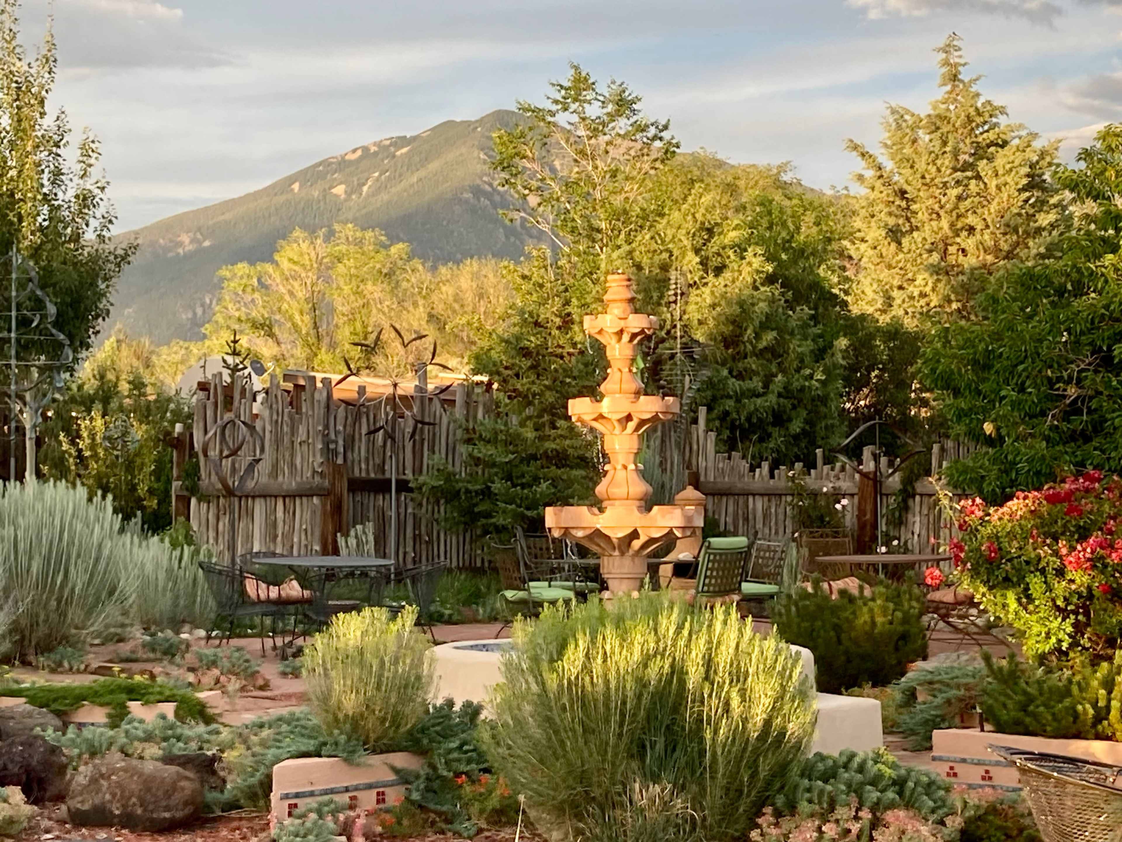A stone fountain stands in a landscaped garden with native plants and a mountain in the background.