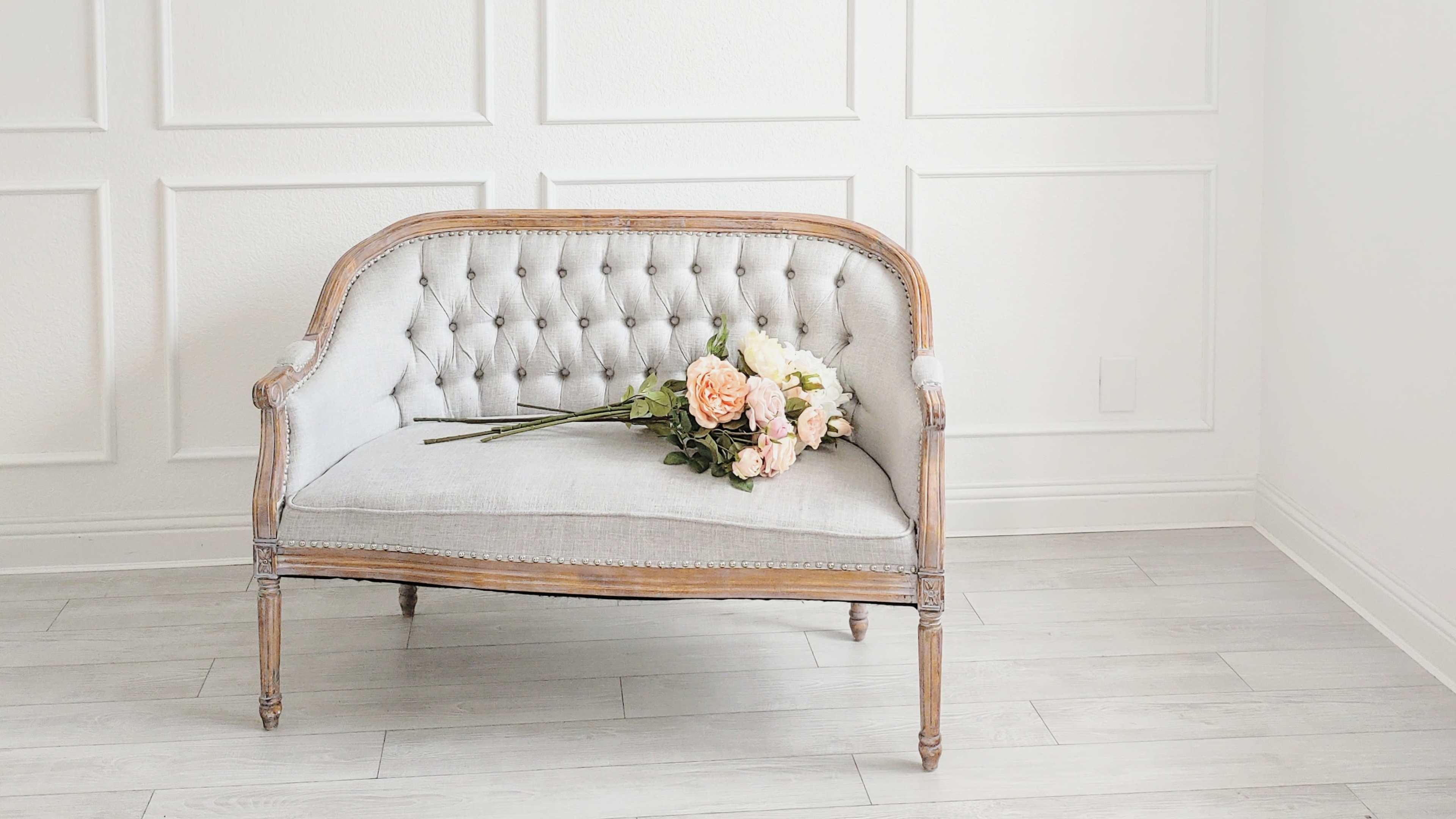 A vintage tufted sofa with a wooden frame sits against a wall, adorned with a bouquet of flowers resting on the seat.